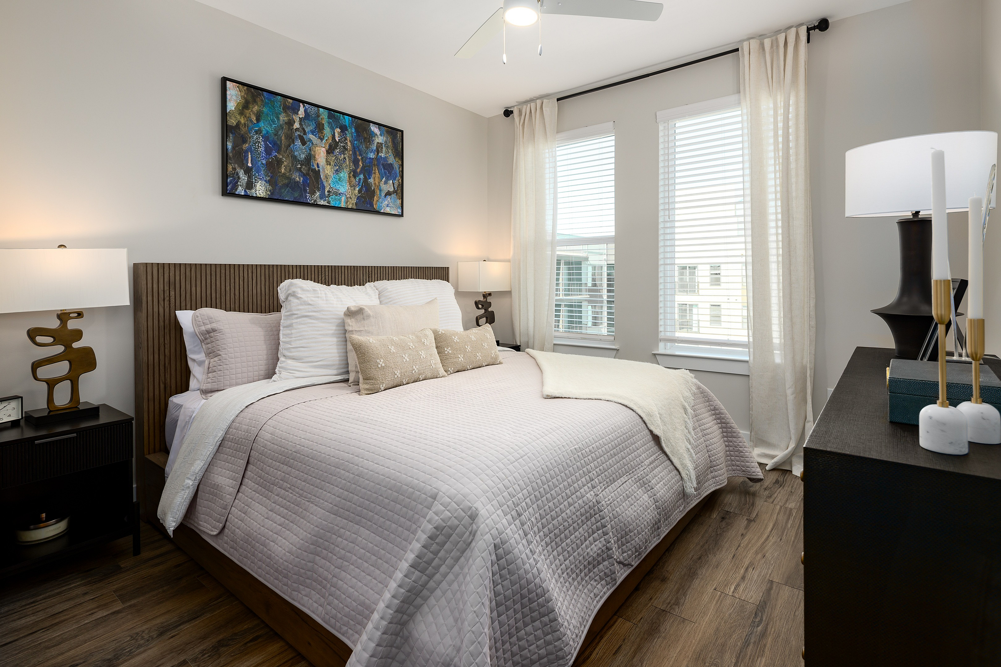 Chic modern bedroom with elegant decor featuring a plush bed, vibrant abstract art, and abundant natural light from large windows.