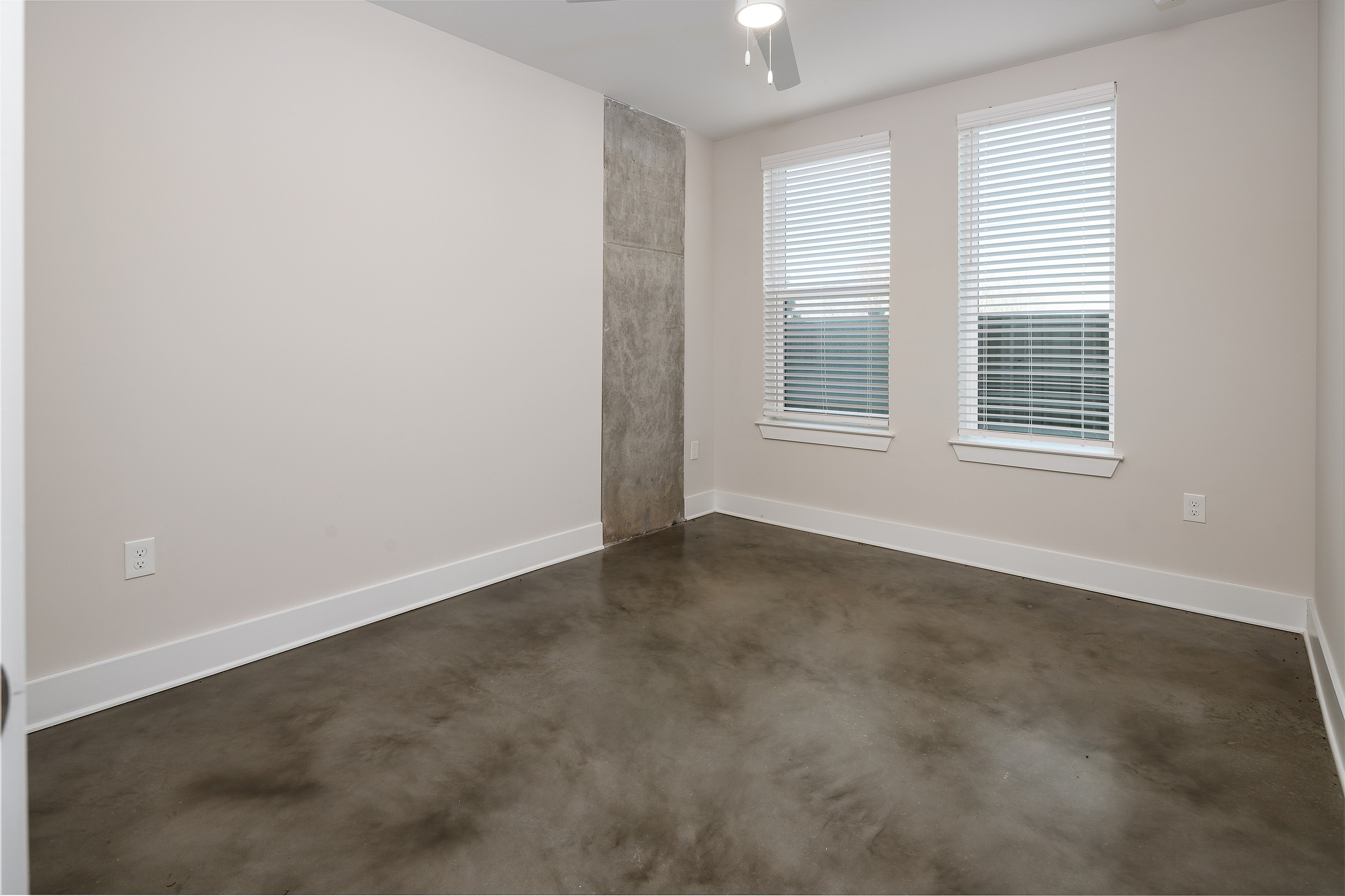 Modern minimalist room with polished concrete floors and bright natural light from two large windows.