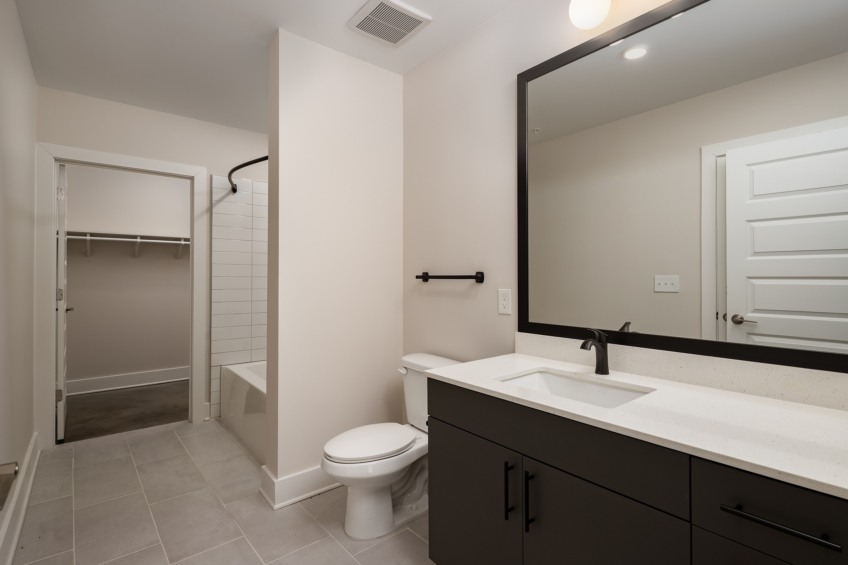 Modern bathroom featuring sleek black cabinetry, elegant white countertops, a large mirror, and a spacious walk-in closet.