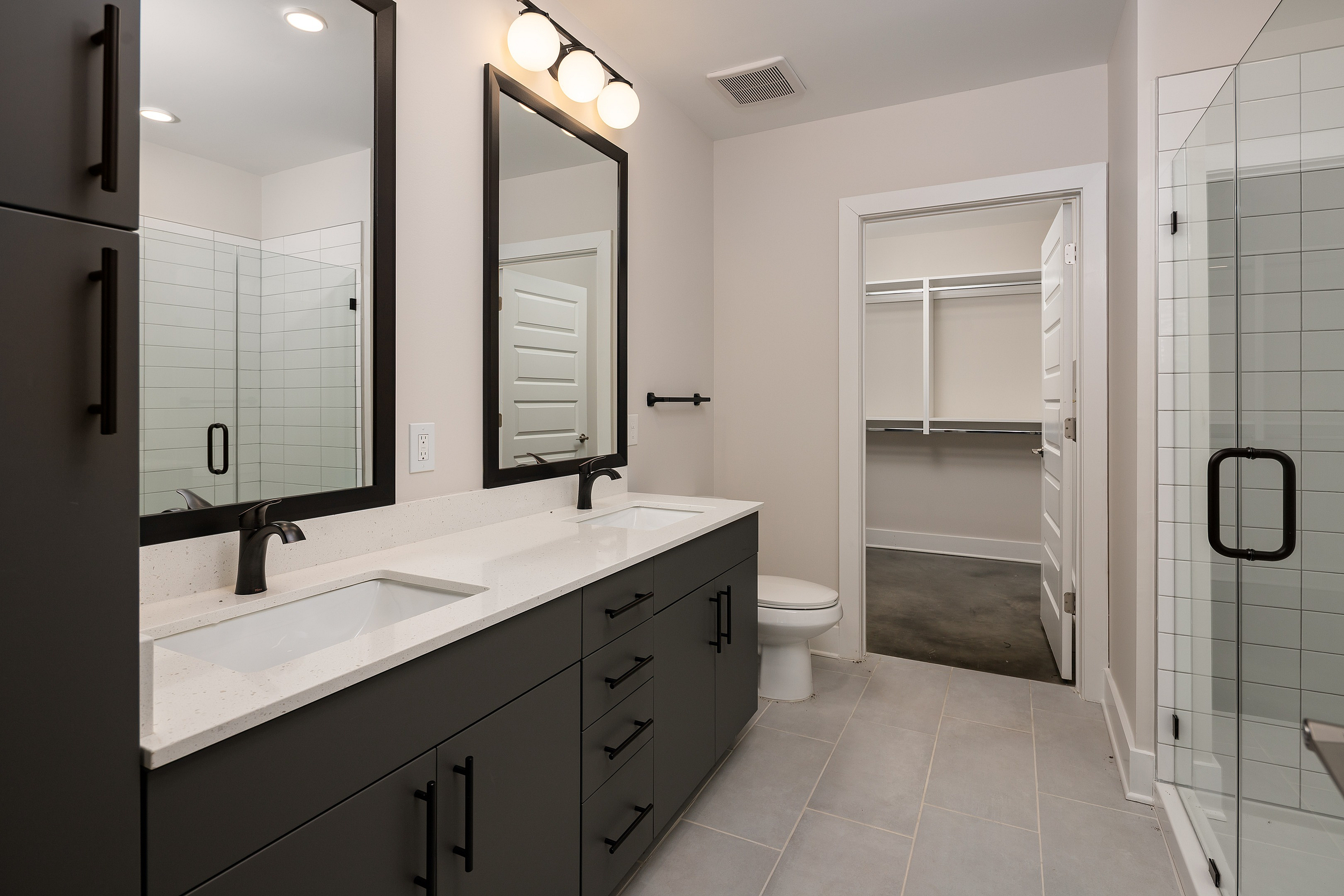 Elegant modern bathroom featuring dual sinks, large mirrors, and a sleek walk-in shower with glass doors, leading to a spacious walk-in closet.