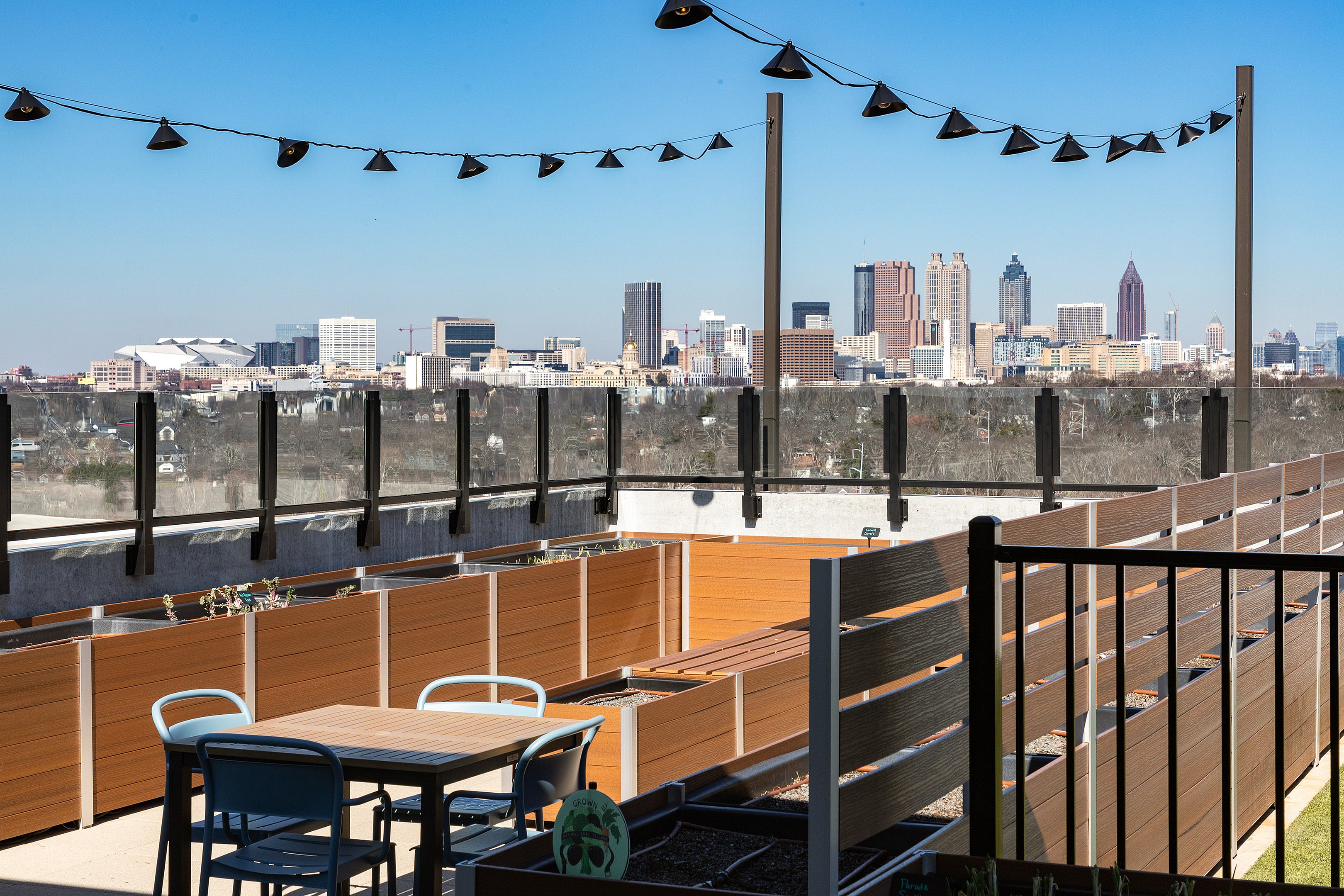 Chic rooftop patio with seating area, modern planters, and breathtaking skyline views under stylish string lights.