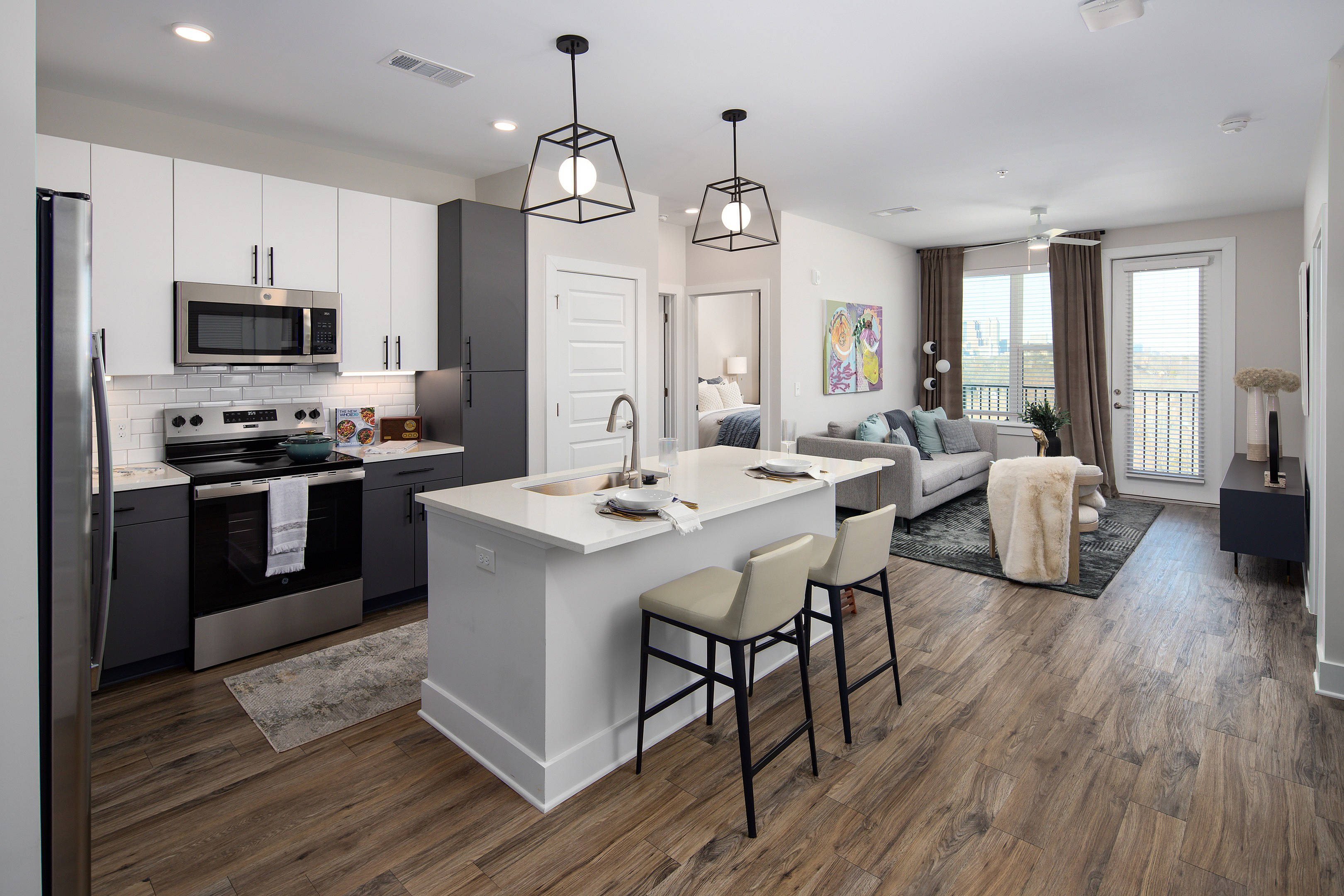 Modern open-plan kitchen and living room with sleek design, featuring elegant lighting, stylish hardwood floors, and a cozy seating area with city views.