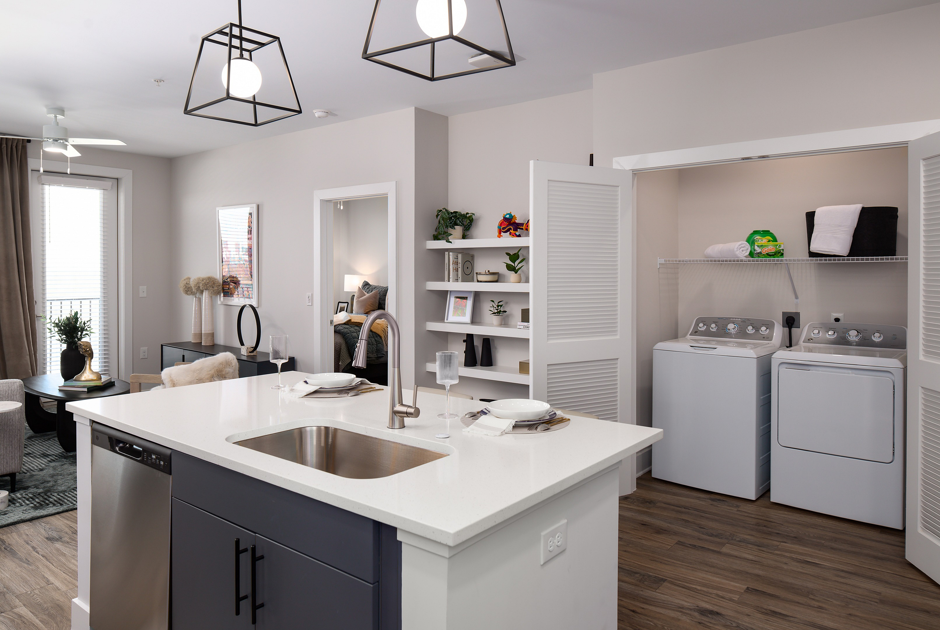 Modern and elegant apartment interior showcasing a chic kitchen island, open living area, and convenient in-unit laundry with stylish shelving accents.