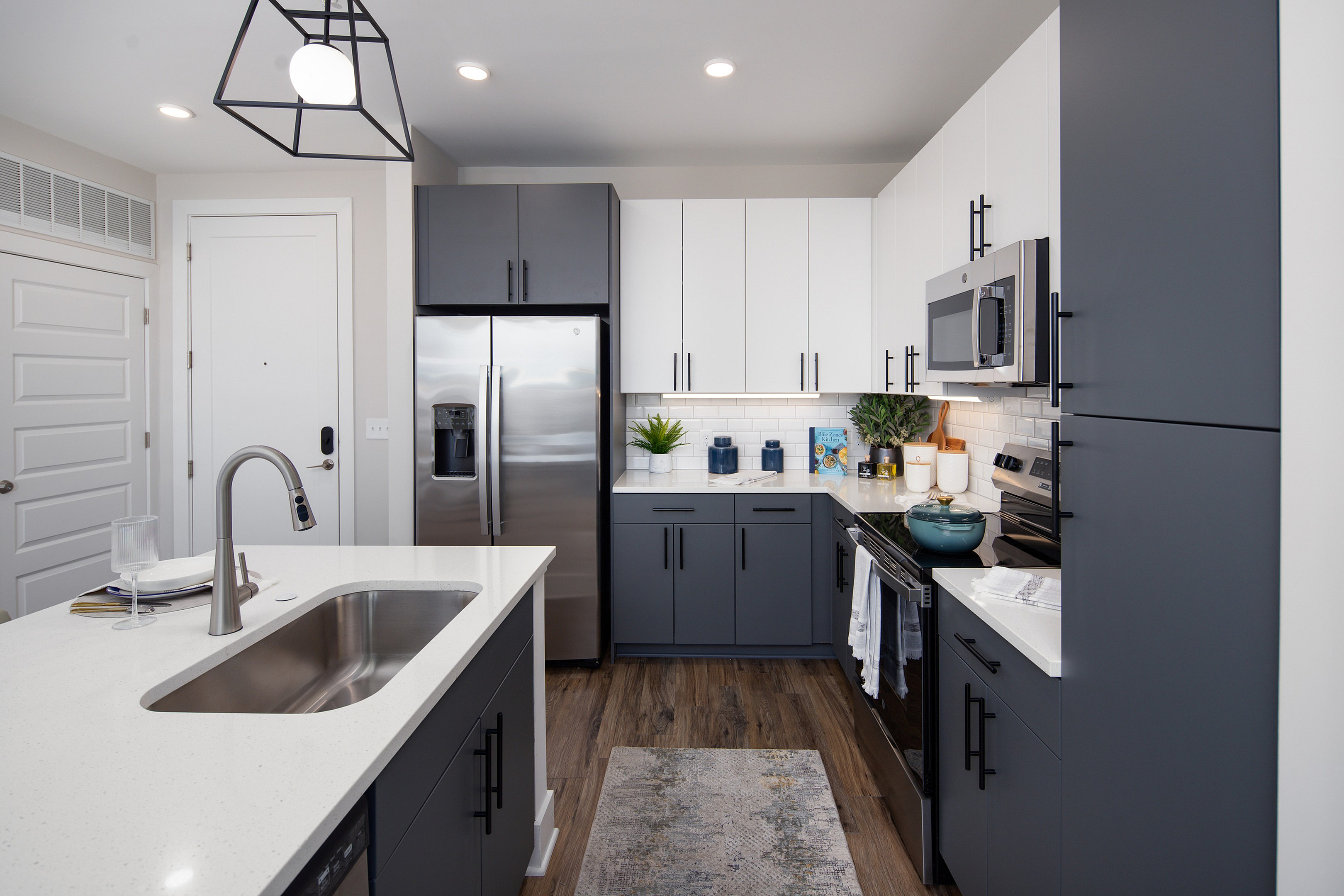 Modern kitchen with sleek cabinetry, stainless steel appliances, and elegant white countertops, featuring stylish pendant lighting and hardwood floors.