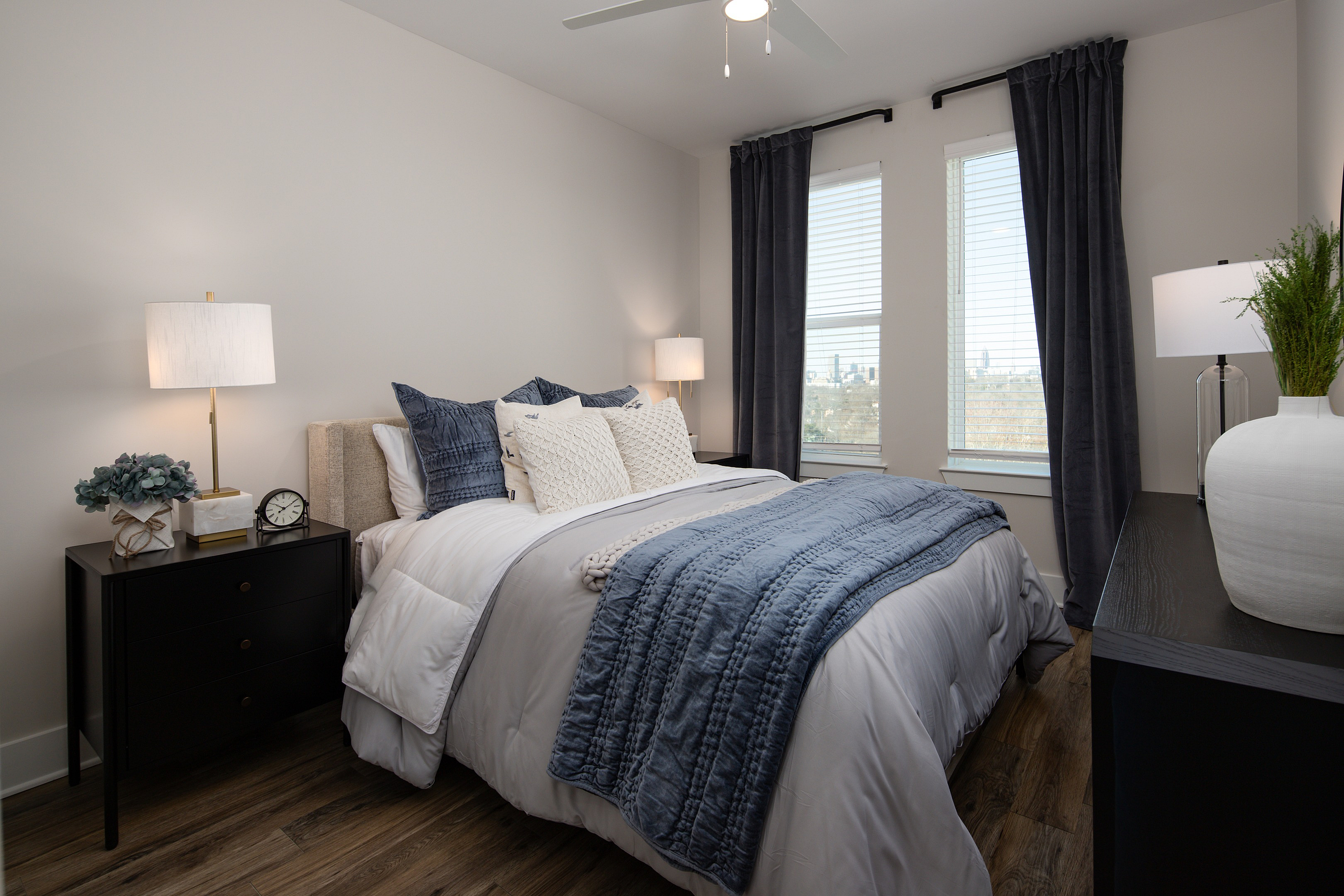 Elegant bedroom with stylish decor, featuring a plush bed with textured pillows, ambient lighting, and large windows with panoramic city views.
