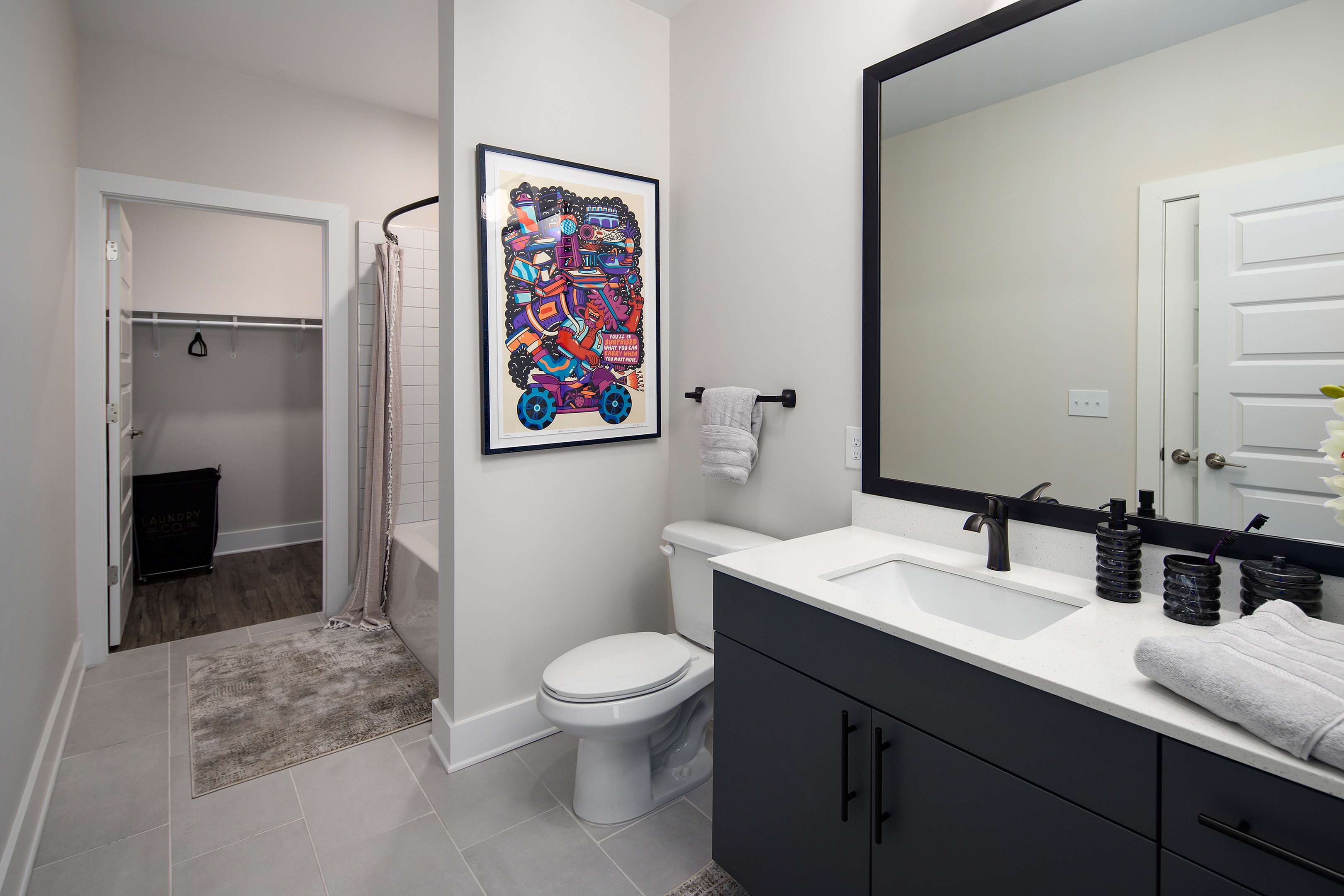 Contemporary bathroom featuring sleek dark cabinetry, modern fixtures, and vibrant wall art, with an inviting shower and ample closet space.
