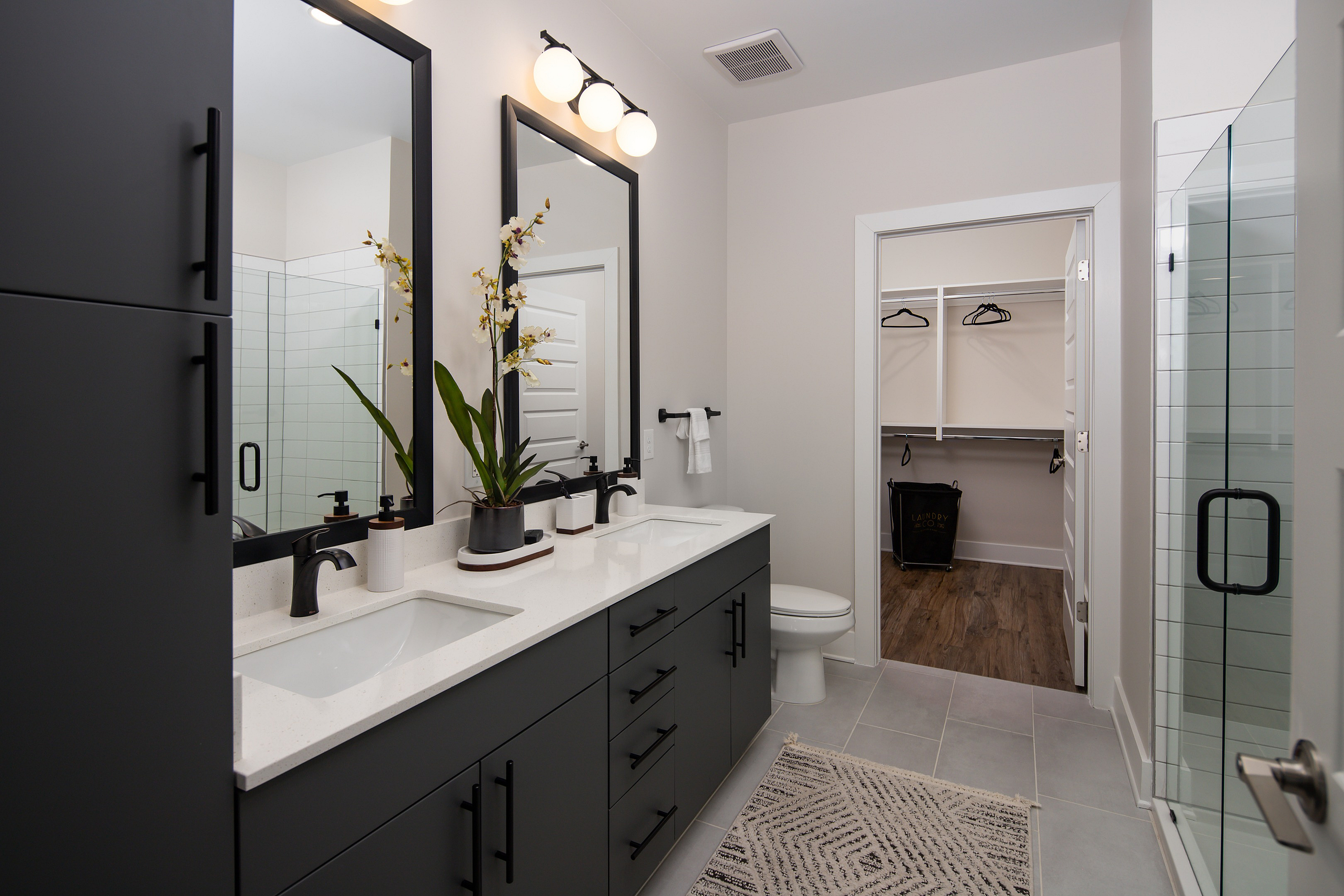 Elegant and modern bathroom with dual sinks, large mirrors, and a bright walk-in closet, featuring stylish black cabinetry and thoughtful decor.