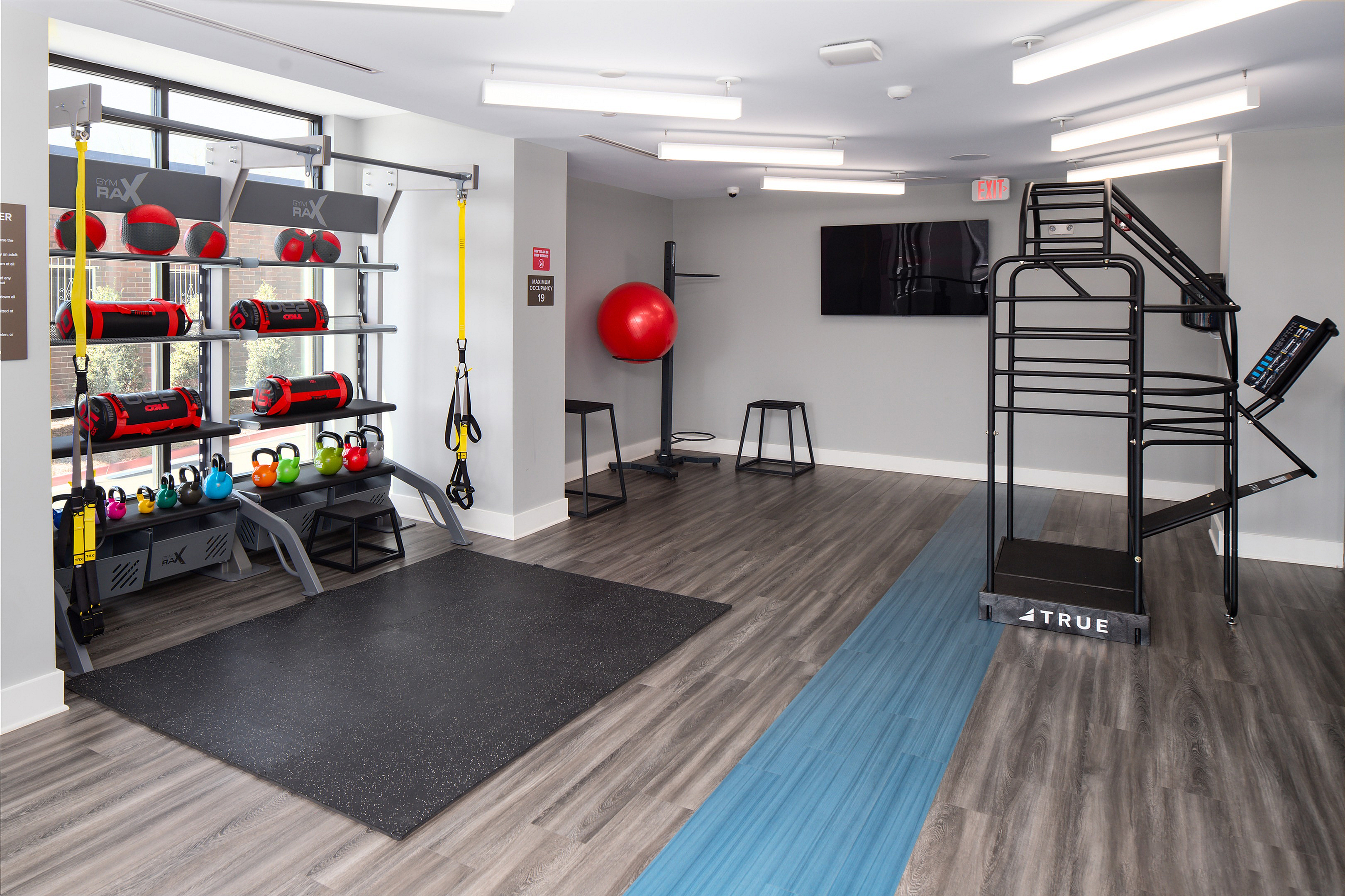 Modern fitness room with sleek hardwood floors, vibrant kettlebells, and versatile exercise equipment; perfect for a dynamic workout experience.