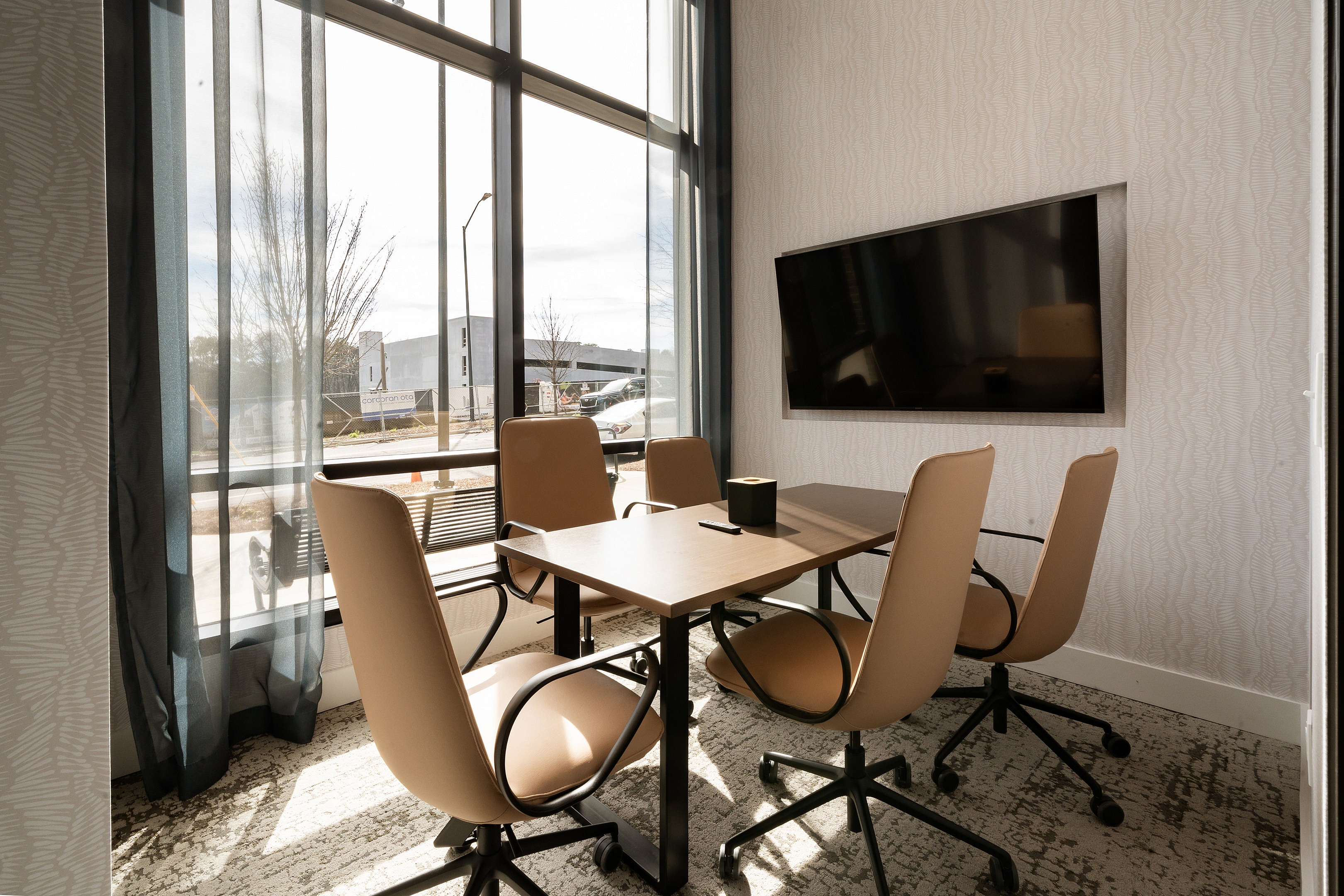 Bright and modern office space with sleek conference table, comfortable chairs, large window, and mounted TV, perfect for productive meetings.