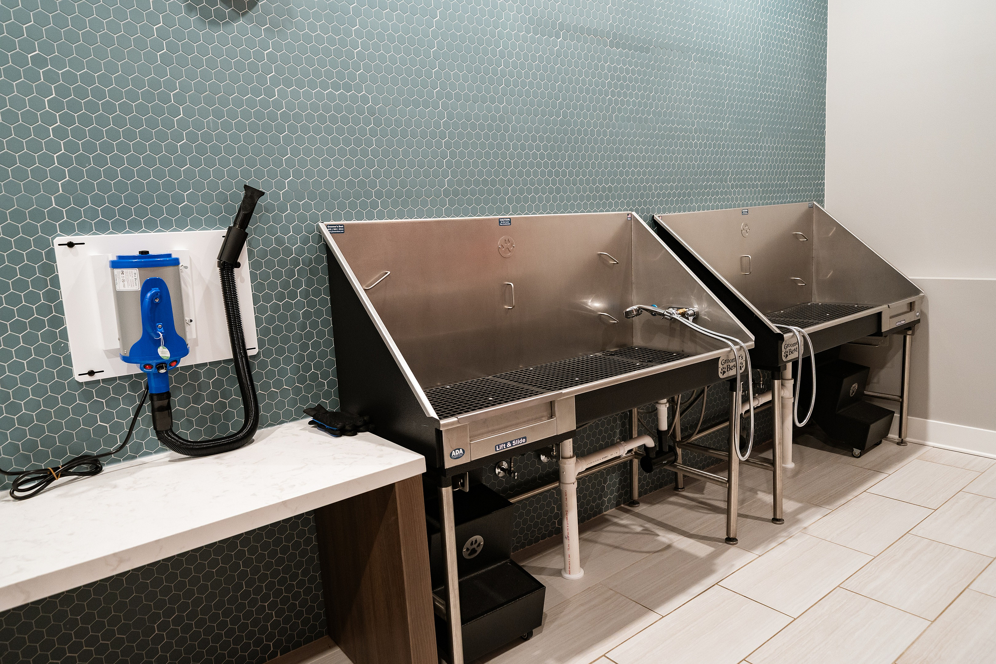 Modern apartment amenity featuring a sleek pet washing station with stainless steel basins and stylish hexagonal tiles.