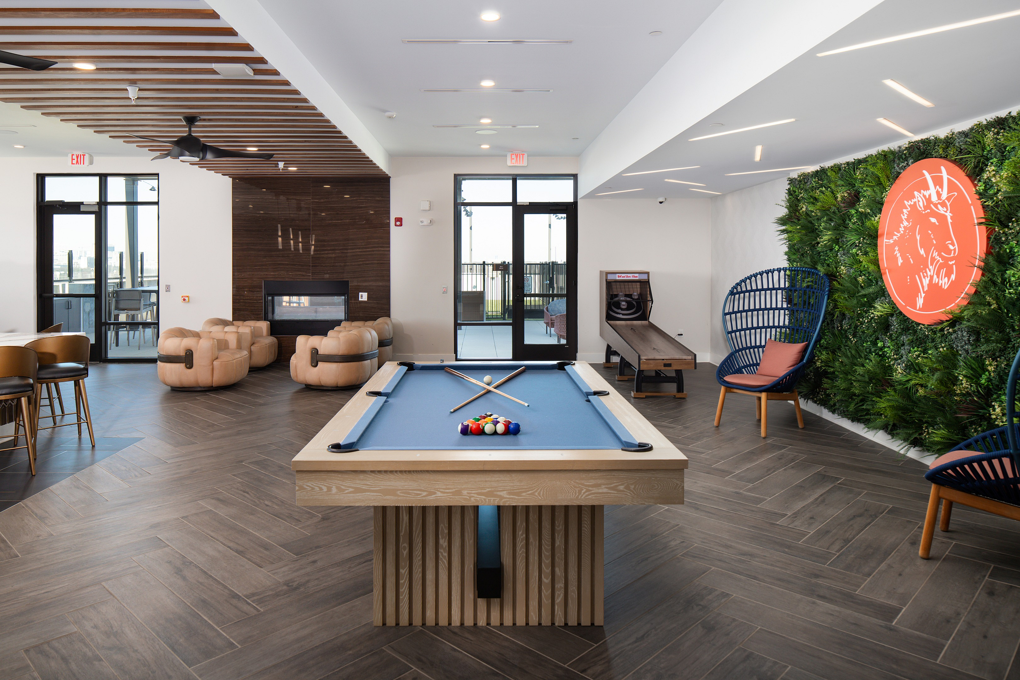 Chic apartment lounge with a modern pool table, cozy seating by a sleek fireplace, and vibrant greenery on the wall, designed for relaxation and entertainment.