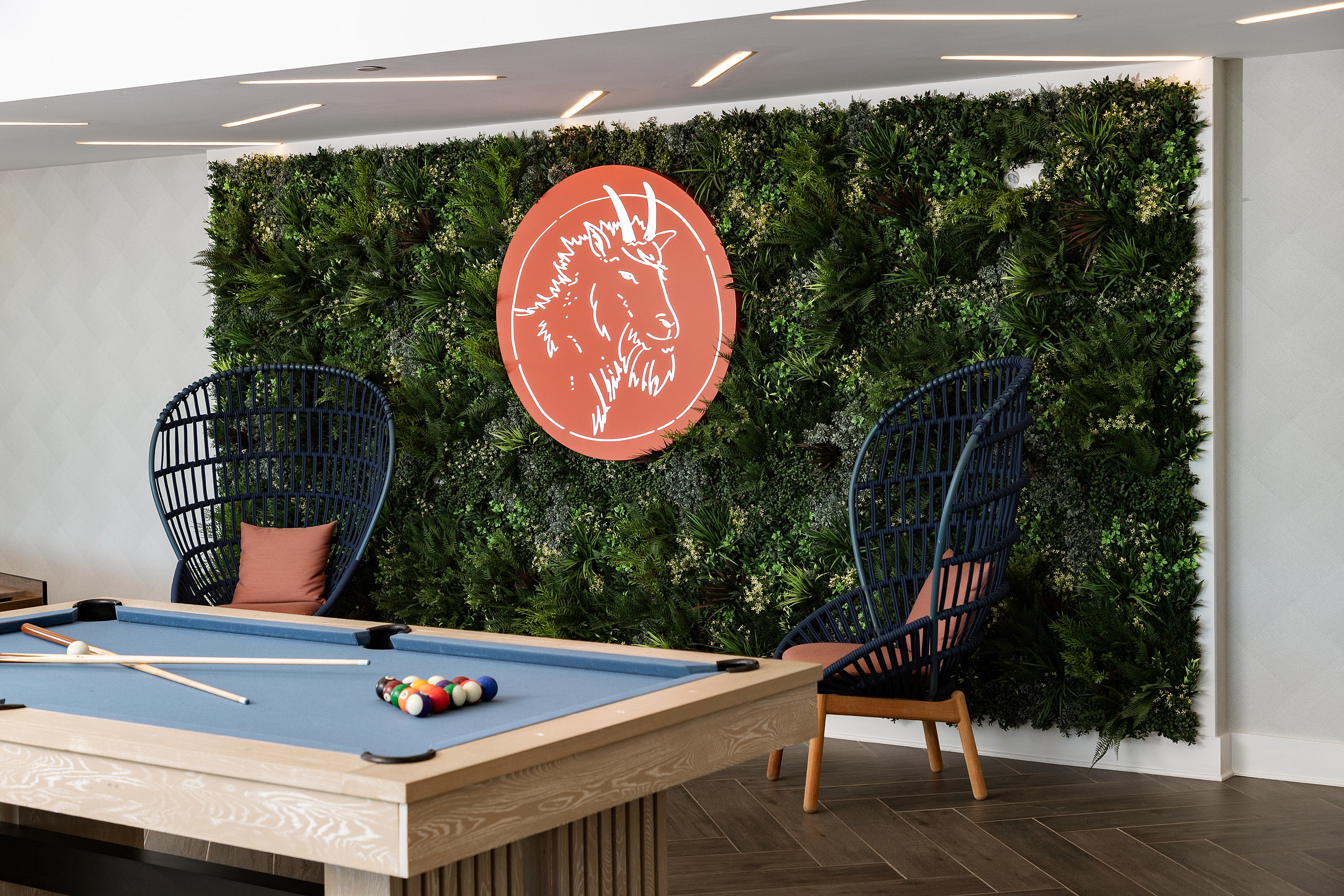 Chic recreational area with a modern billiards table, stylish rattan chairs, and a lush green wall featuring a striking art piece.