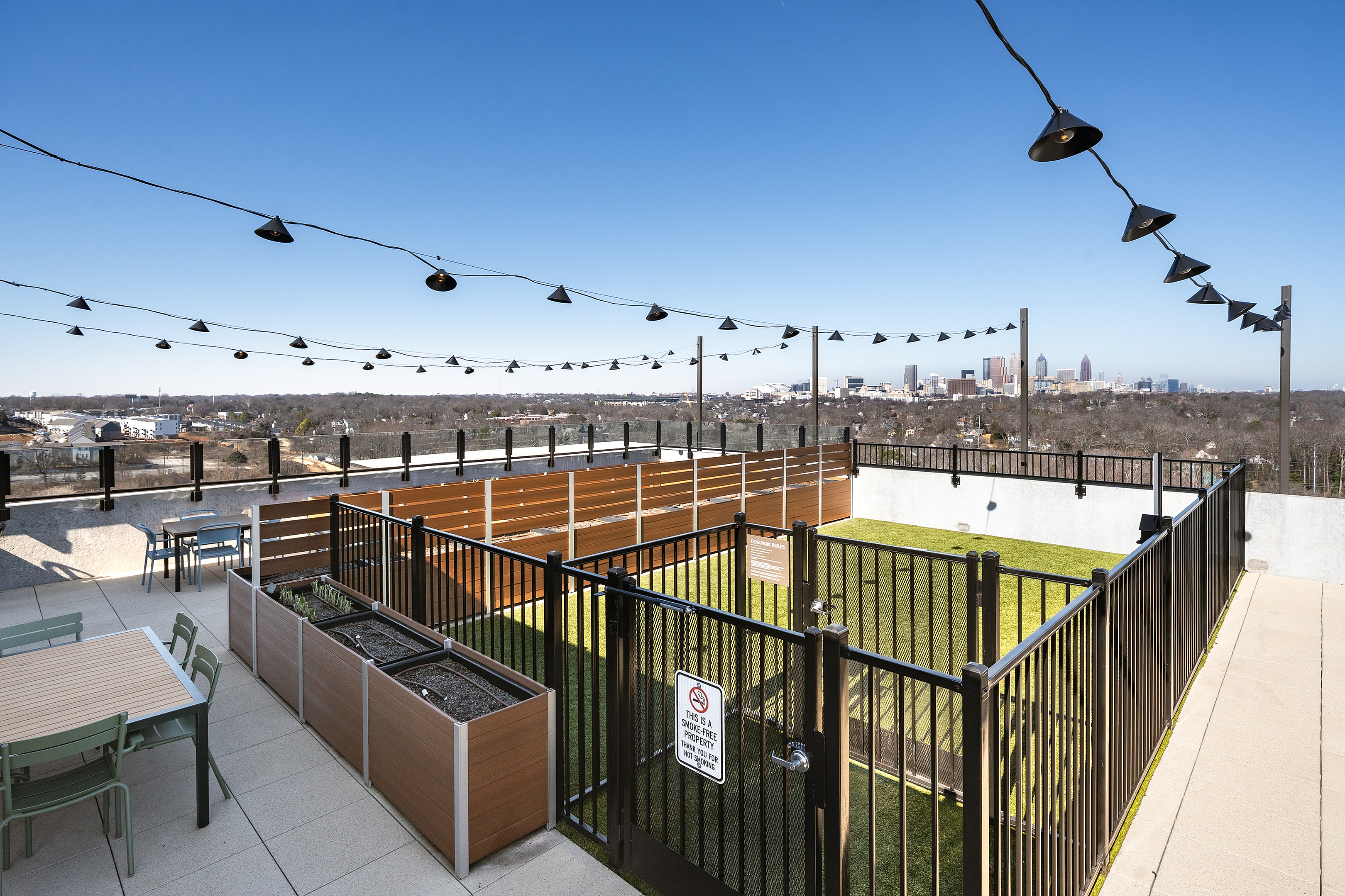 Charming rooftop patio with string lights, cozy seating, and stunning city views on a bright day.