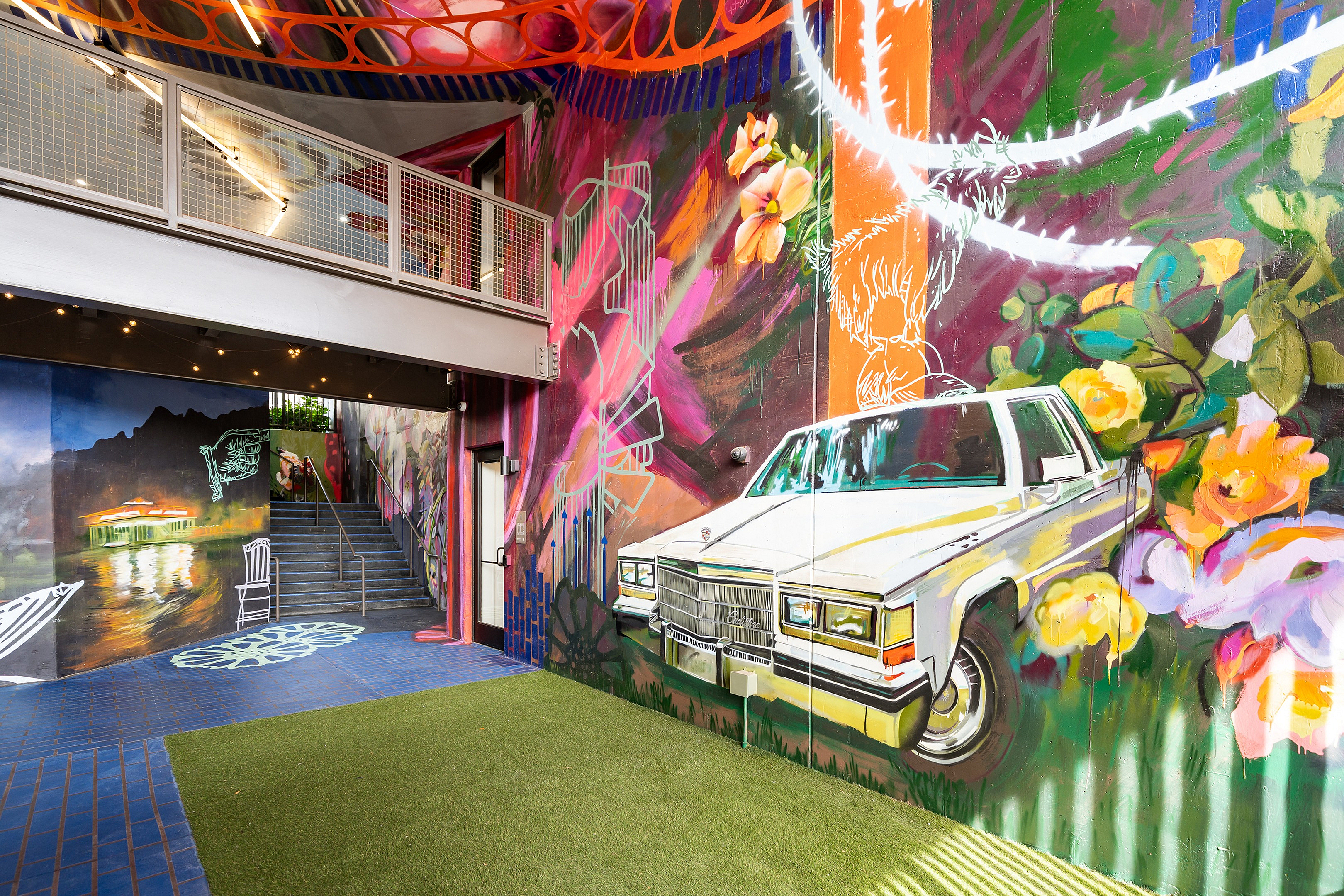 Vibrant urban art space featuring colorful graffiti with a classic car mural, lush greenery, and a chic modern staircase.