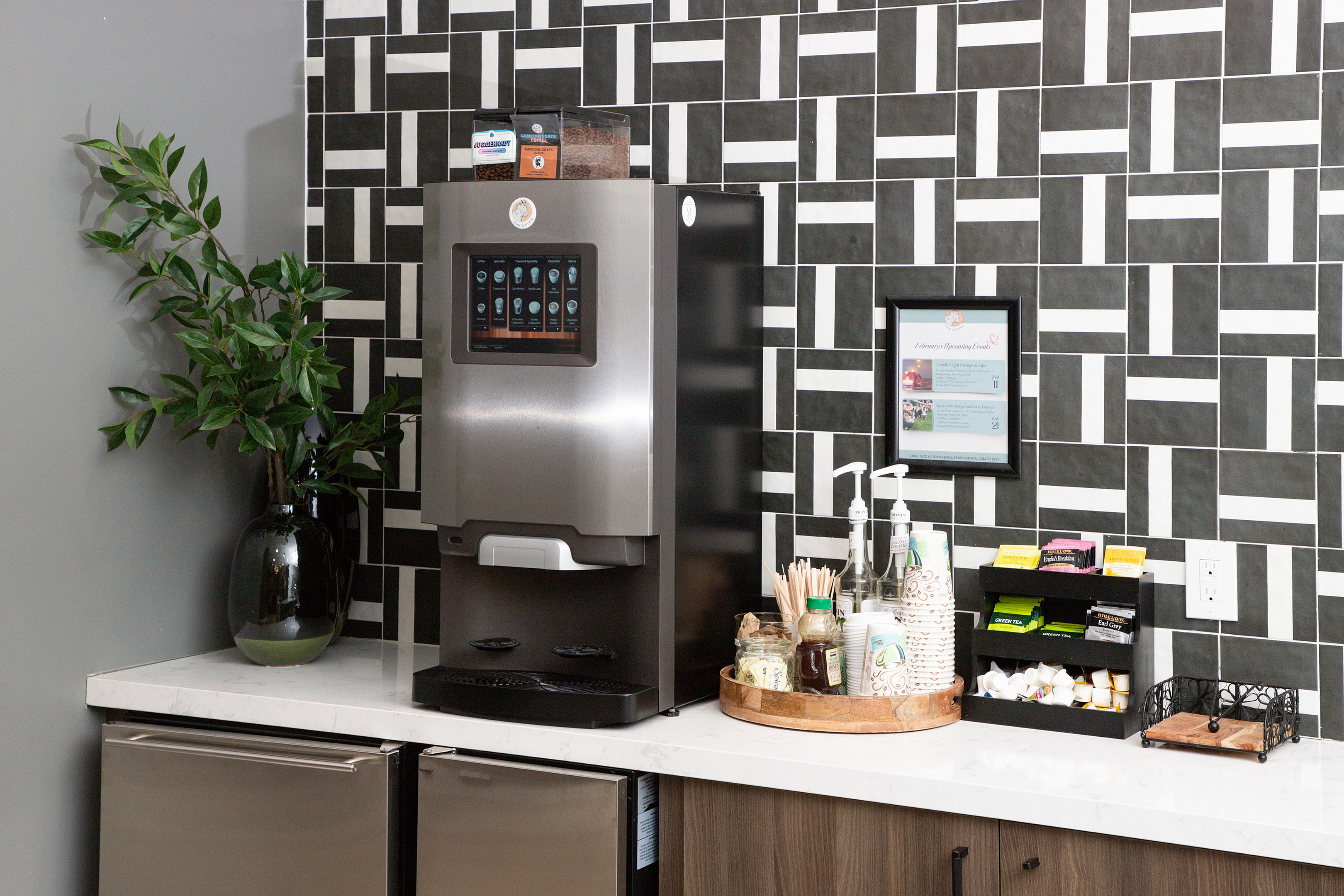 Sleek kitchen corner featuring a modern coffee machine, stylish geometric backsplash, and an elegant countertop setup with cups and condiments.