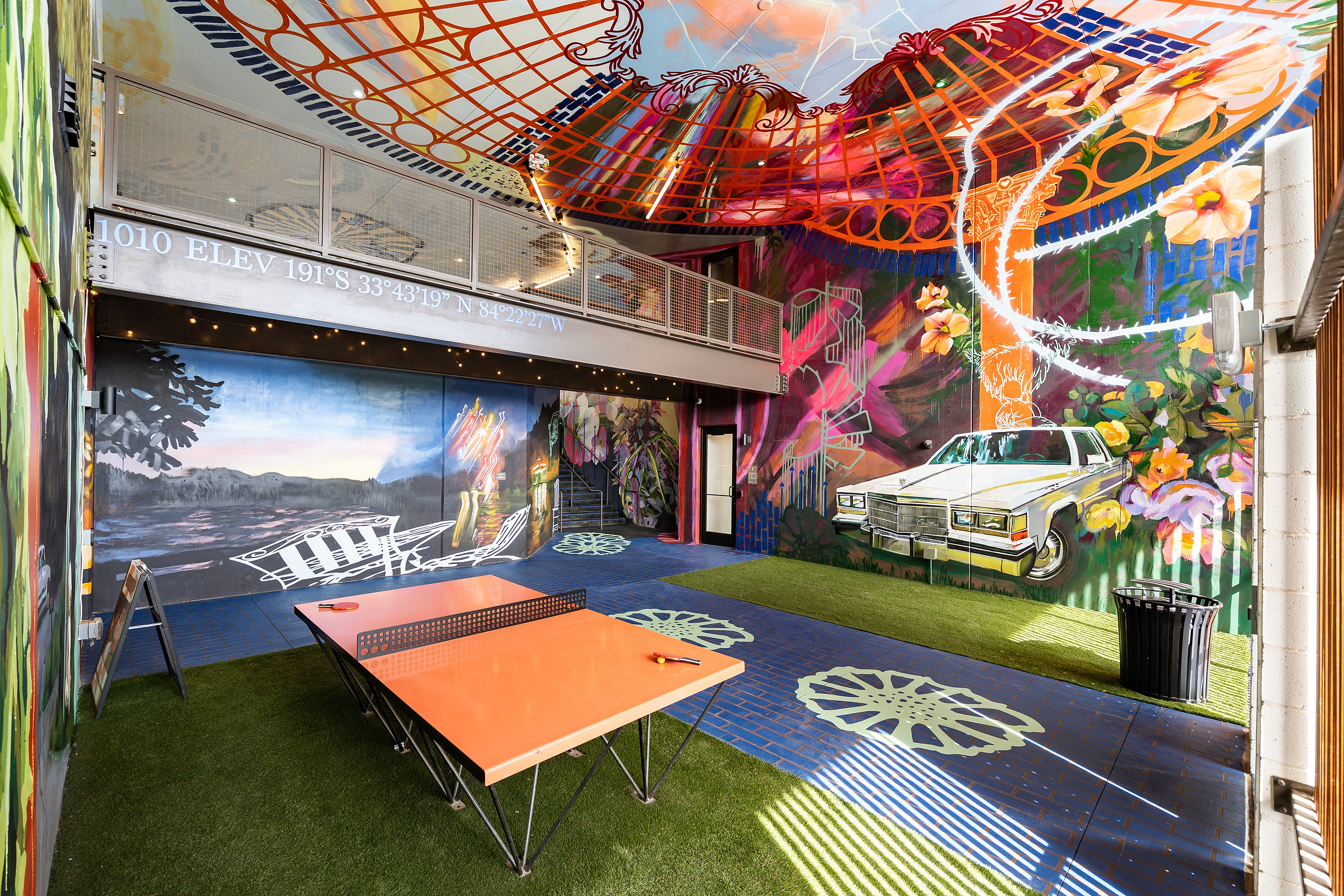 Vibrant indoor space featuring colorful murals, an orange ping pong table, and green artificial grass, creating a playful and artistic atmosphere.
