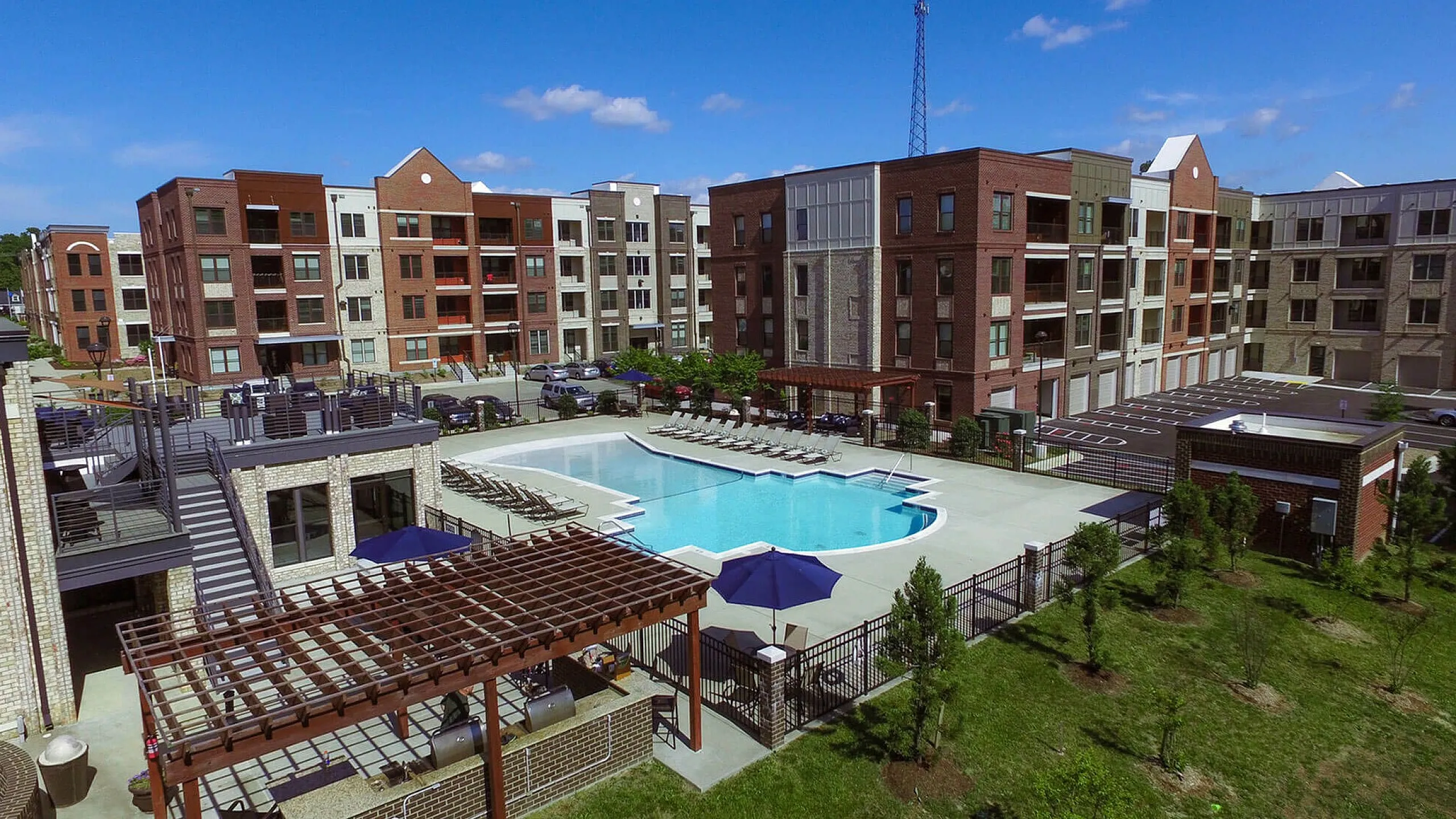 Modern brick apartment complex with large swimming pool and outdoor seating area.