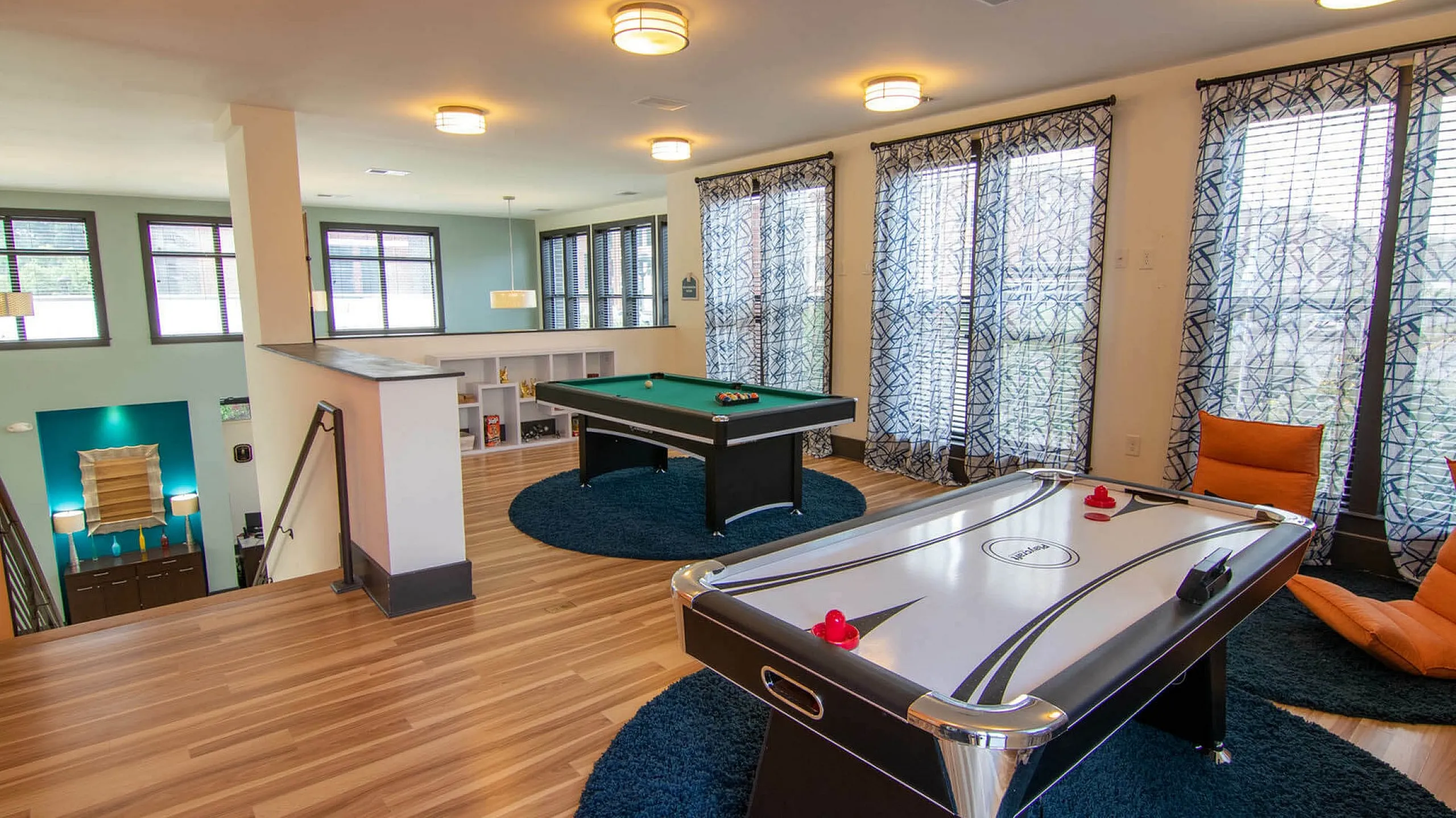Spacious apartment game room featuring a pool table and air hockey with modern decor and large windows.