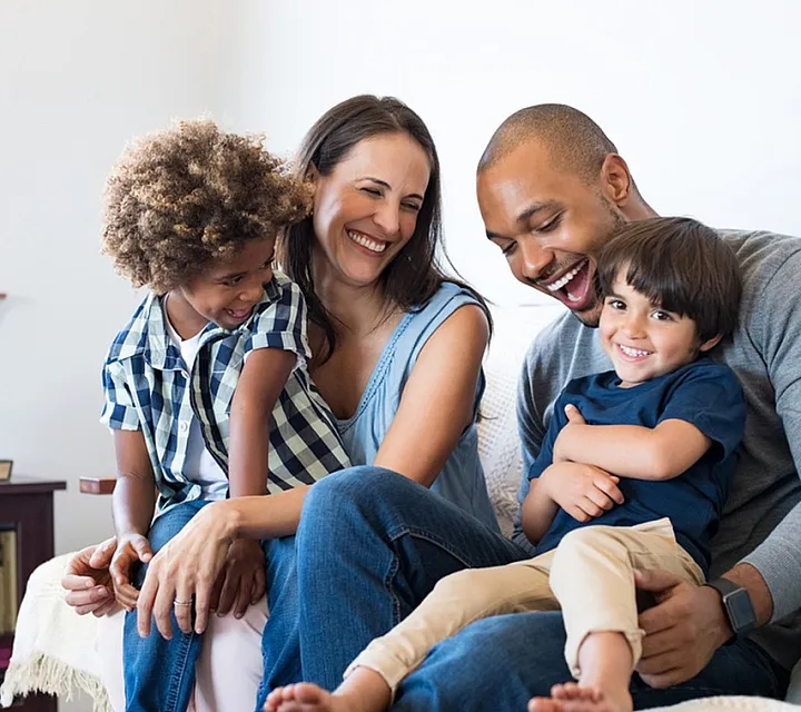 Joyful family sitting on a cozy sofa in a bright living room with books and plants.