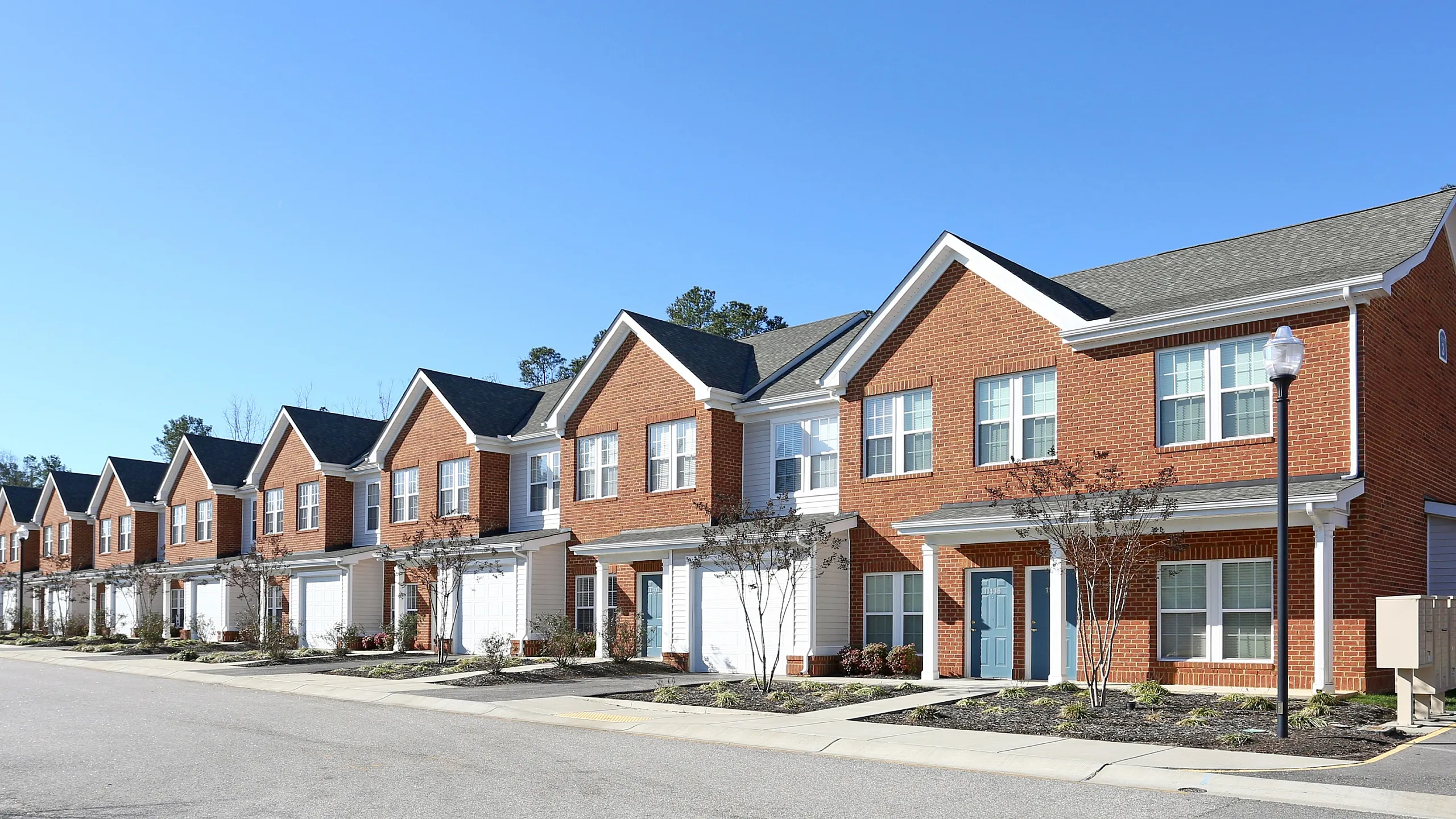 Beautiful row of red-brick townhomes with blue doors in a tranquil suburban neighborhood under a clear sky.