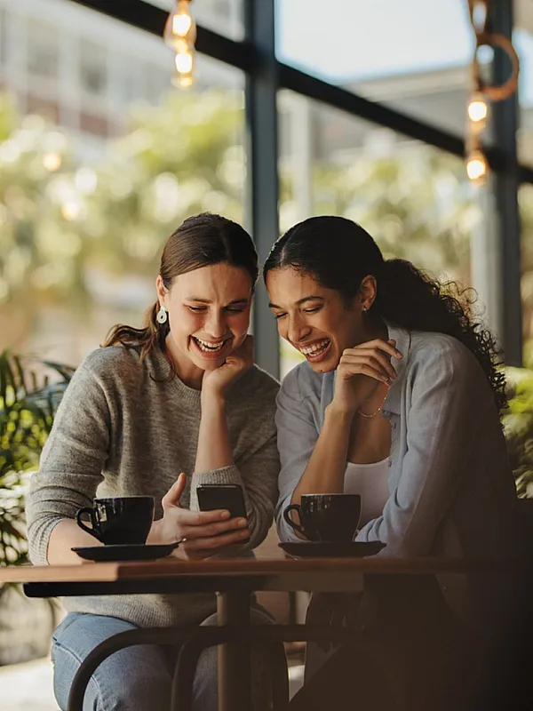 Two friends enjoying coffee and laughter in a bright, cozy cafe.