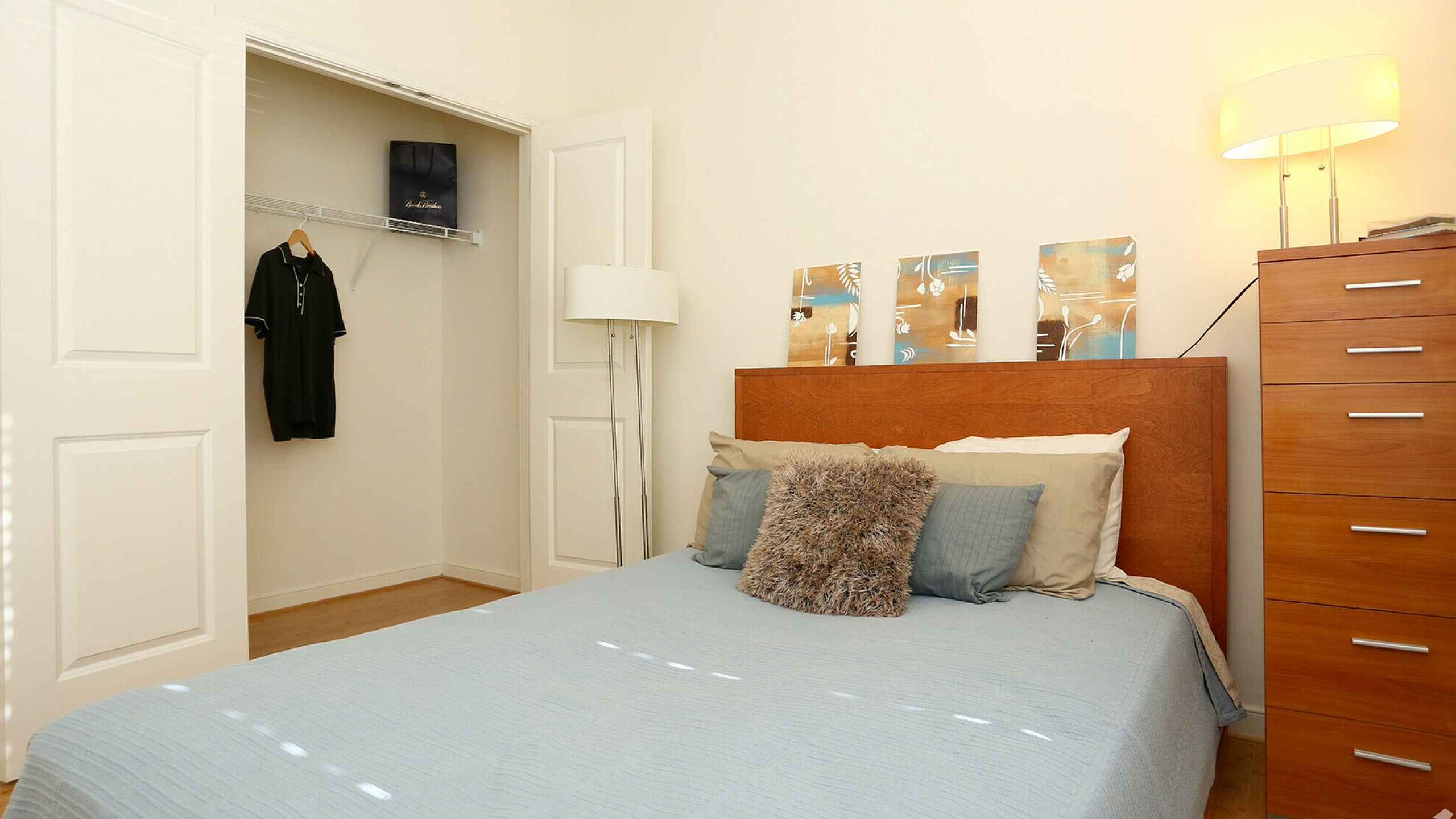 Inviting bedroom with a blue bedspread, wooden dresser, and closet space, warmly lit.