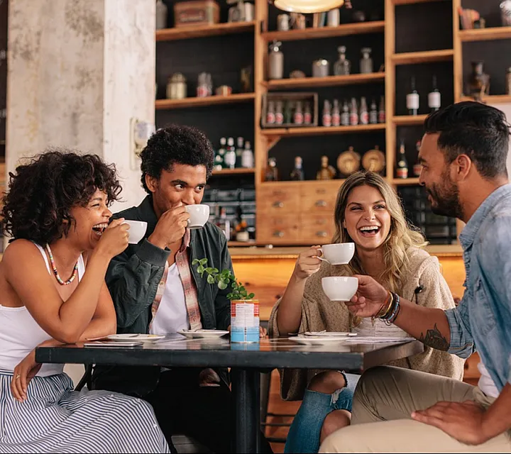 Cheerful group of friends enjoying coffee and conversation at a cozy cafe with rustic decor.
