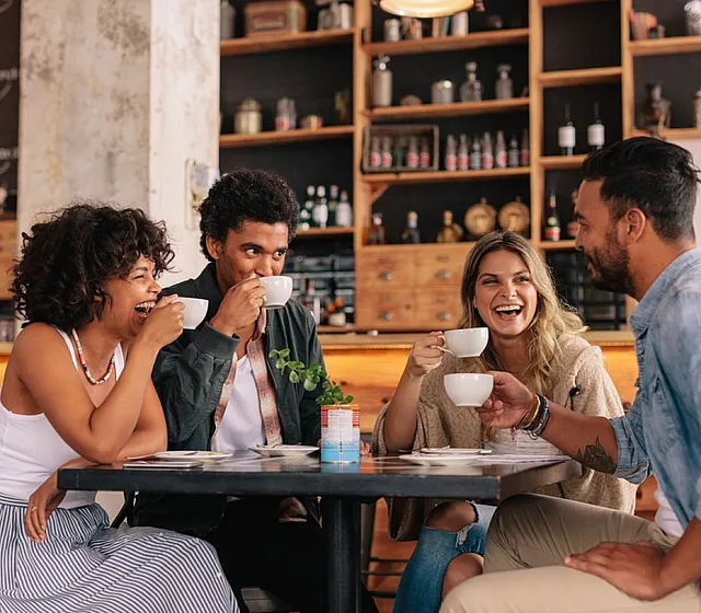 Group of friends enjoying coffee and laughter at a stylish urban caf&eacute;.