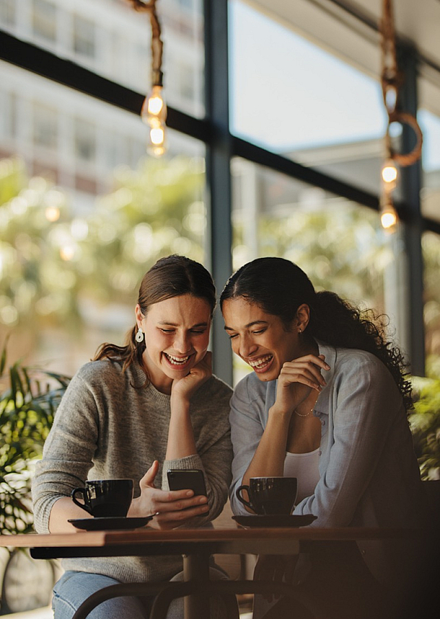 Two friends enjoying a coffee break in a cozy cafe with large windows.