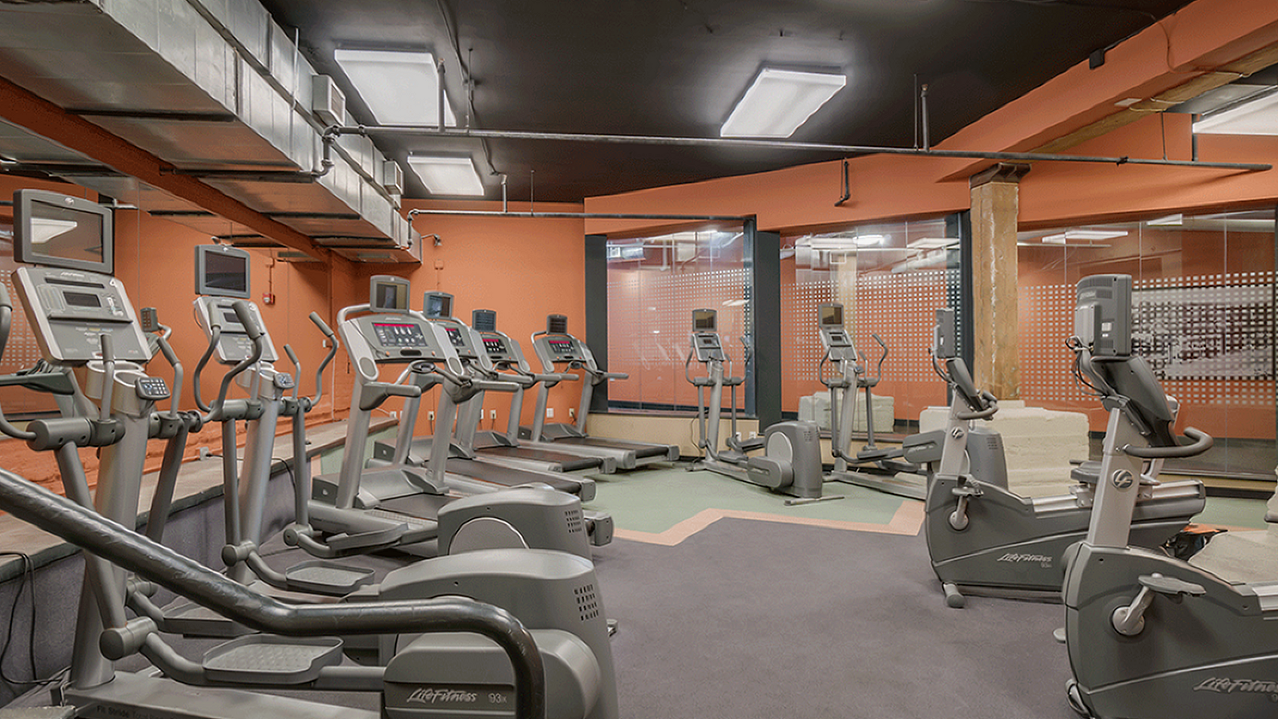 Modern gym with a variety of exercise machines and vibrant orange accents.