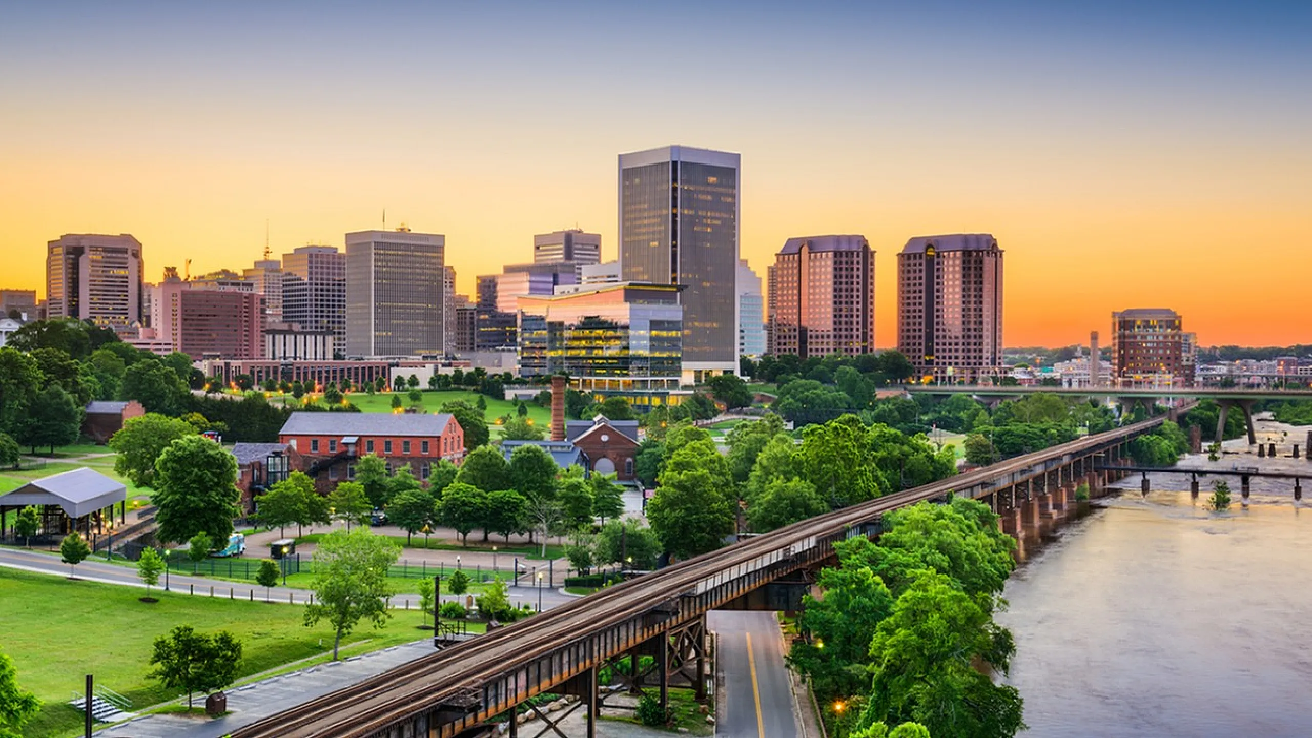 Vibrant city skyline at sunset with lush greenery and a tranquil river.