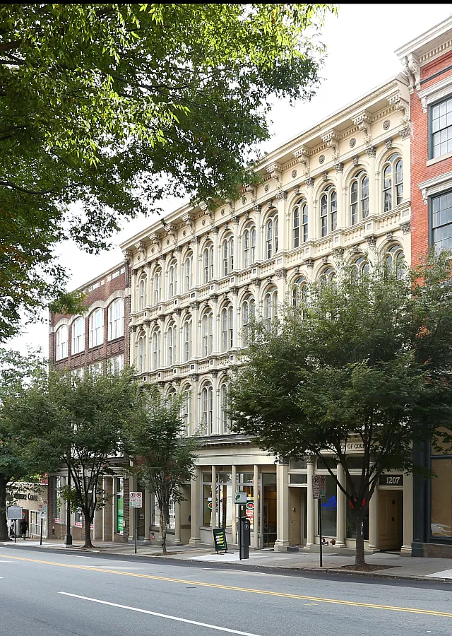 Street view of elegant historic buildings with classic architectural details and lush trees lining the street.