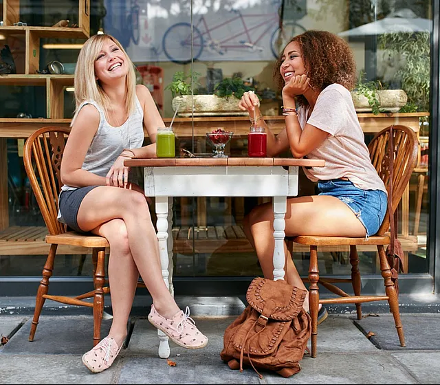 Two women enjoy colorful smoothies at a stylish outdoor cafe.