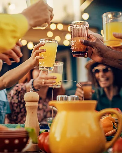 A vibrant group of friends toasting with glasses of orange juice at a lively outdoor gathering.