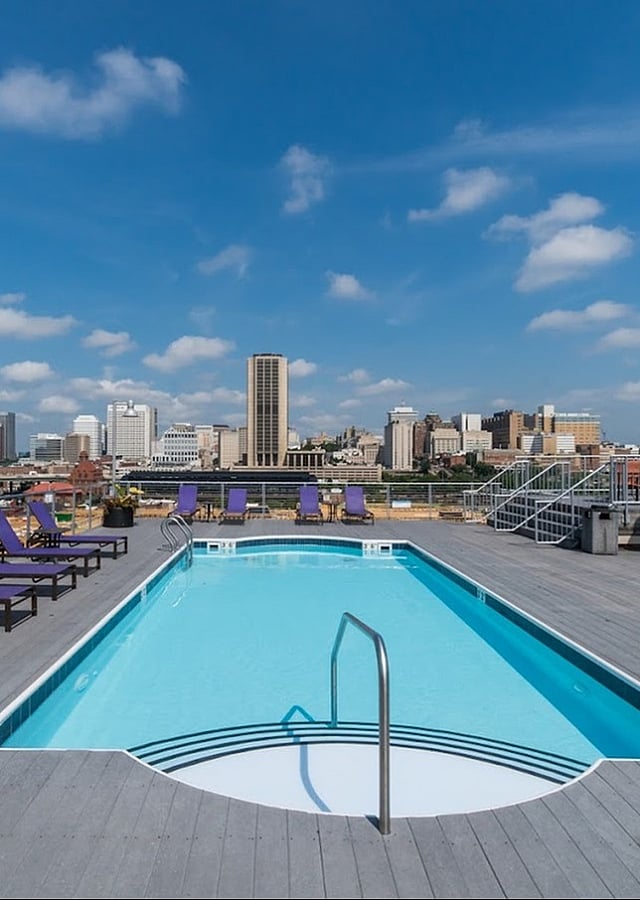 Inviting rooftop pool with lounge chairs overlooking a vibrant city skyline on a sunny day.