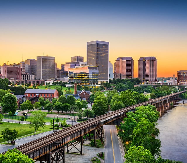 Scenic view of a vibrant city skyline at sunset with lush greenery and a tranquil river.