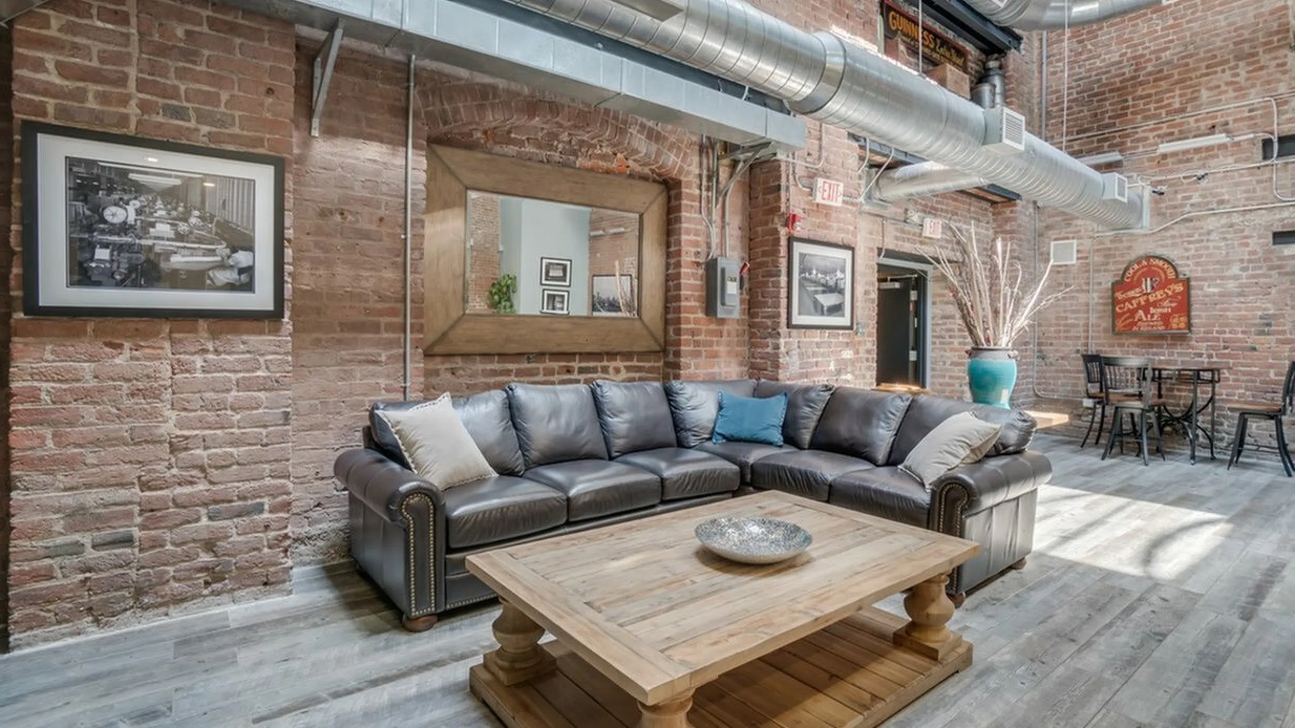 Cozy industrial-style living room with exposed brick, leather sectional sofa, and rustic wood coffee table.