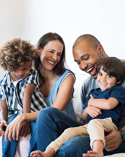 Happy family of four laughing together on a cozy sofa in a bright living room.