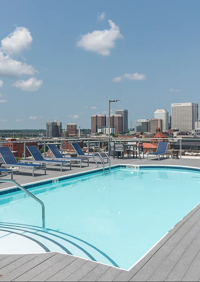 Rooftop swimming pool with modern lounge chairs and stunning city skyline view.