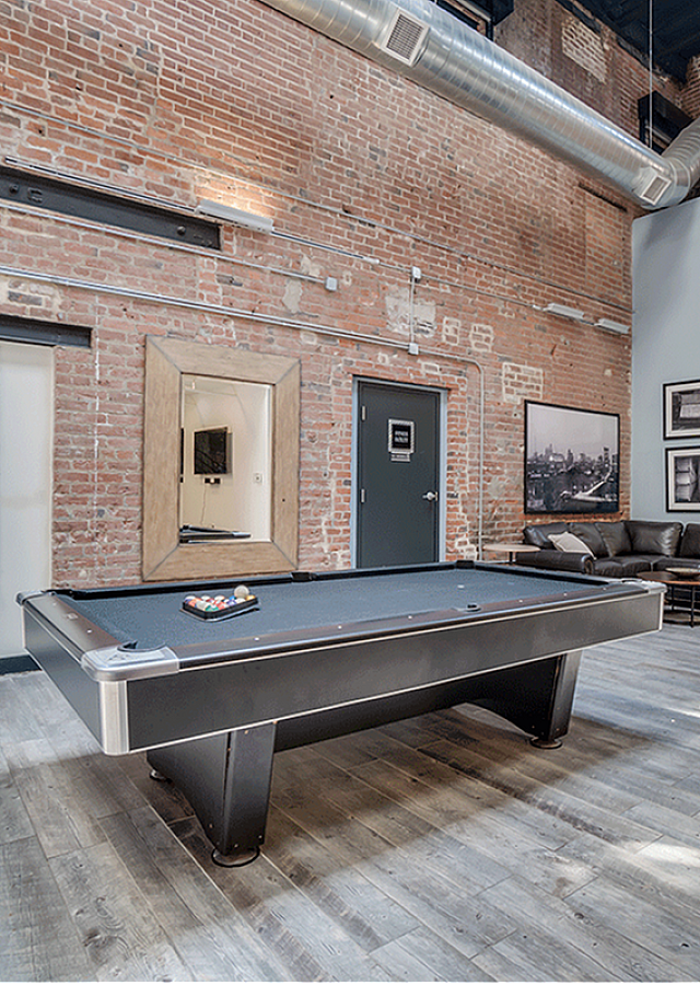 Chic loft-style recreation room featuring an industrial design with exposed brick walls and a pool table.