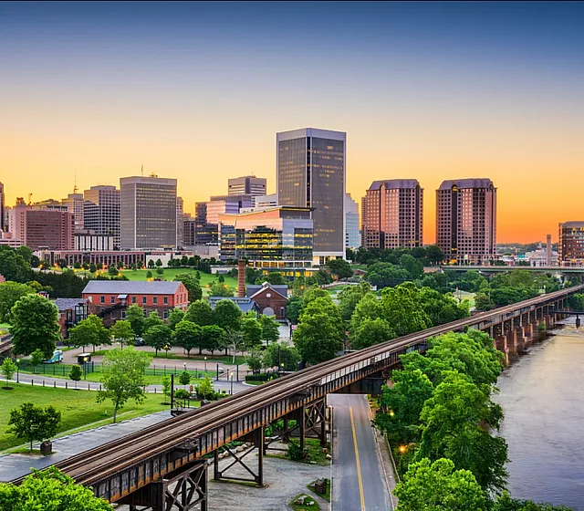 Panoramic view of a city skyline at sunset with vibrant green parks and a river.