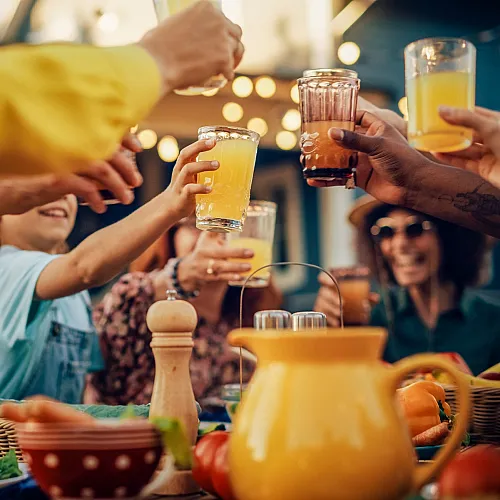 Cheerful group having a toast with colorful drinks at an outdoor table loaded with fresh food.