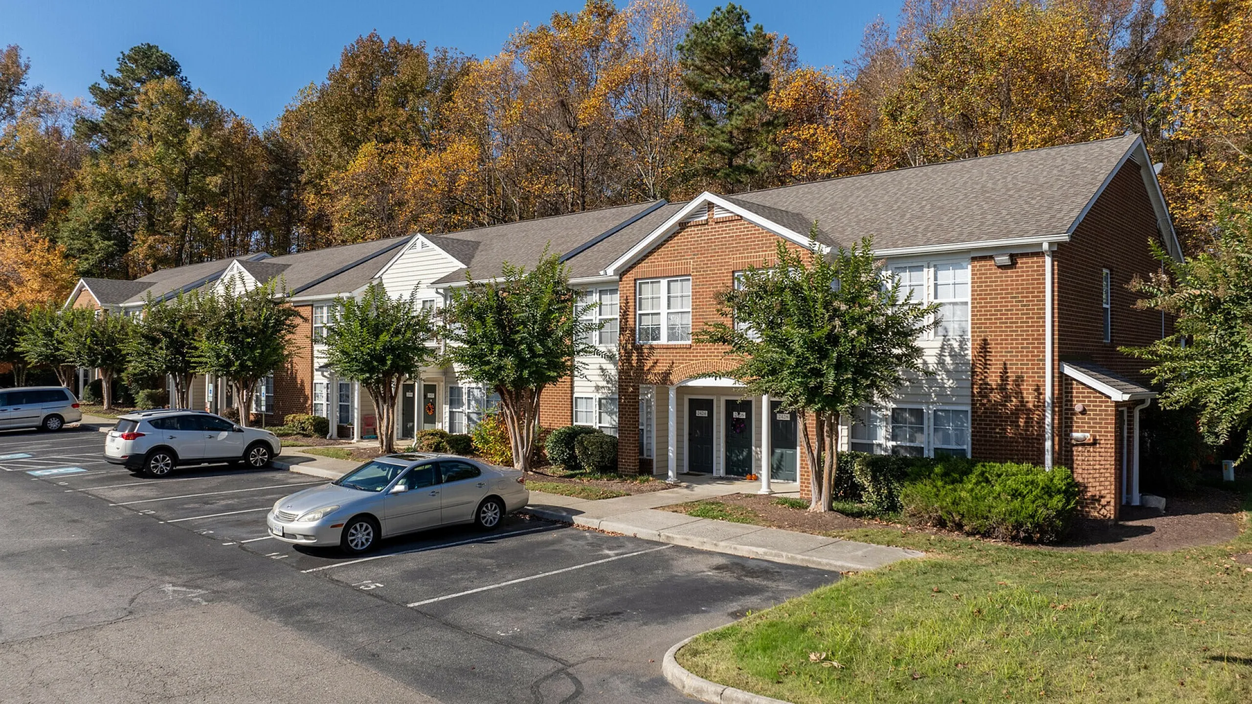 Sunny autumn view of a charming townhouse complex with ample parking and lush trees.