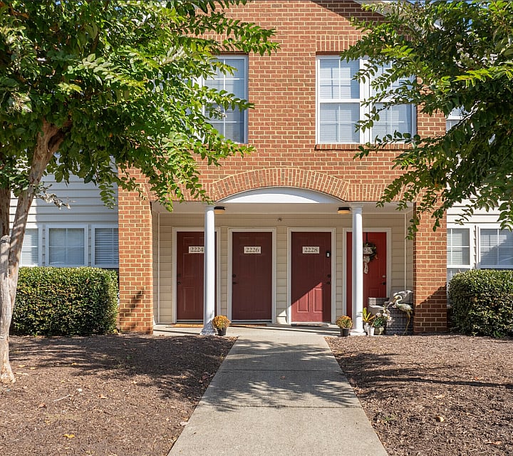 Welcoming brick facade with red doors surrounded by greenery and white columns.
