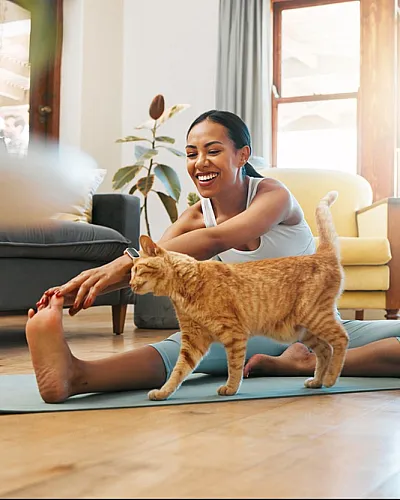 Woman practicing yoga with a cat in a bright and cozy living room.