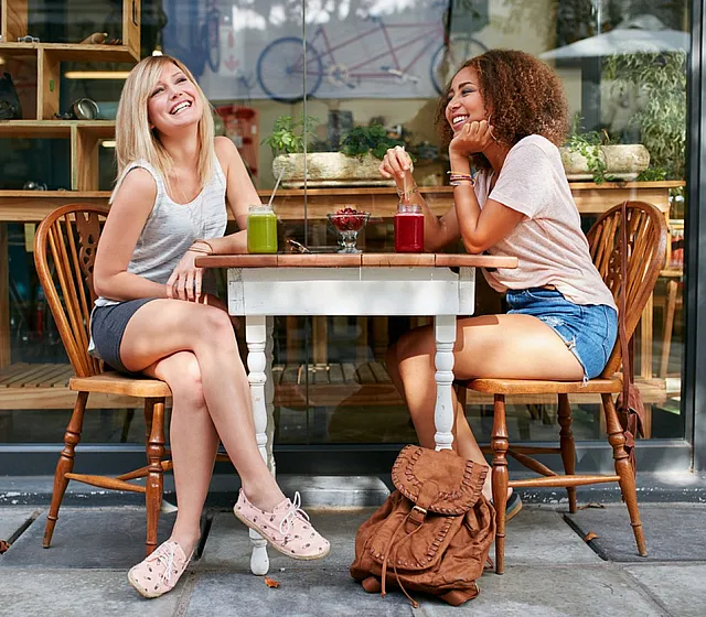 Two women enjoying fresh juices at an outdoor cafe, surrounded by a warm and cozy atmosphere.