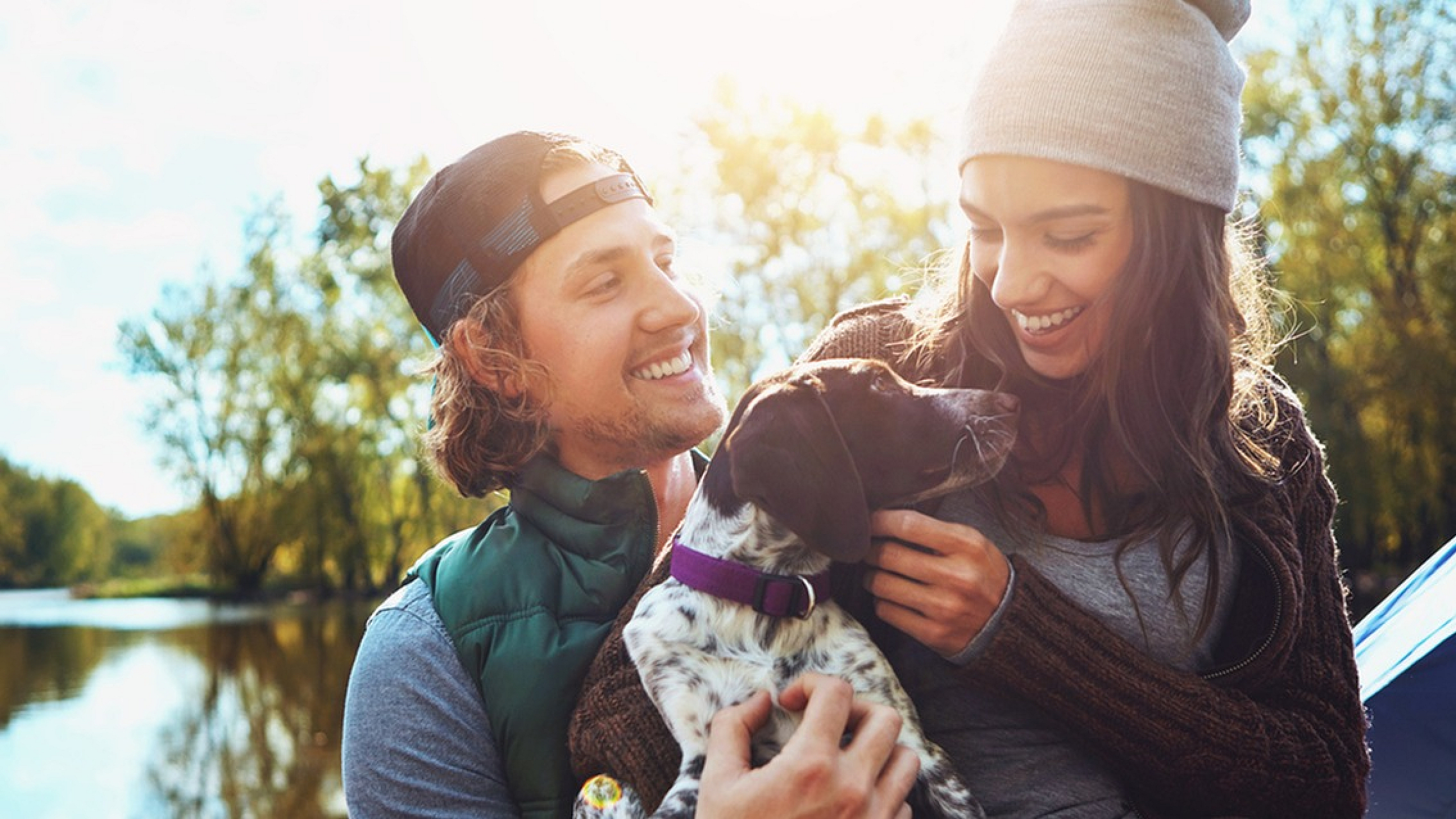 Happy couple enjoying a sunny day by the river with their dog.
