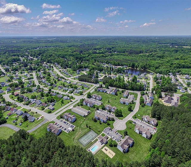 Aerial view of a picturesque suburban neighborhood surrounded by lush greenery and featuring a central swimming pool and tennis court.