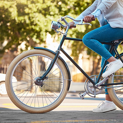 Person enjoying a city ride on a vintage bicycle, surrounded by sunny greenery.