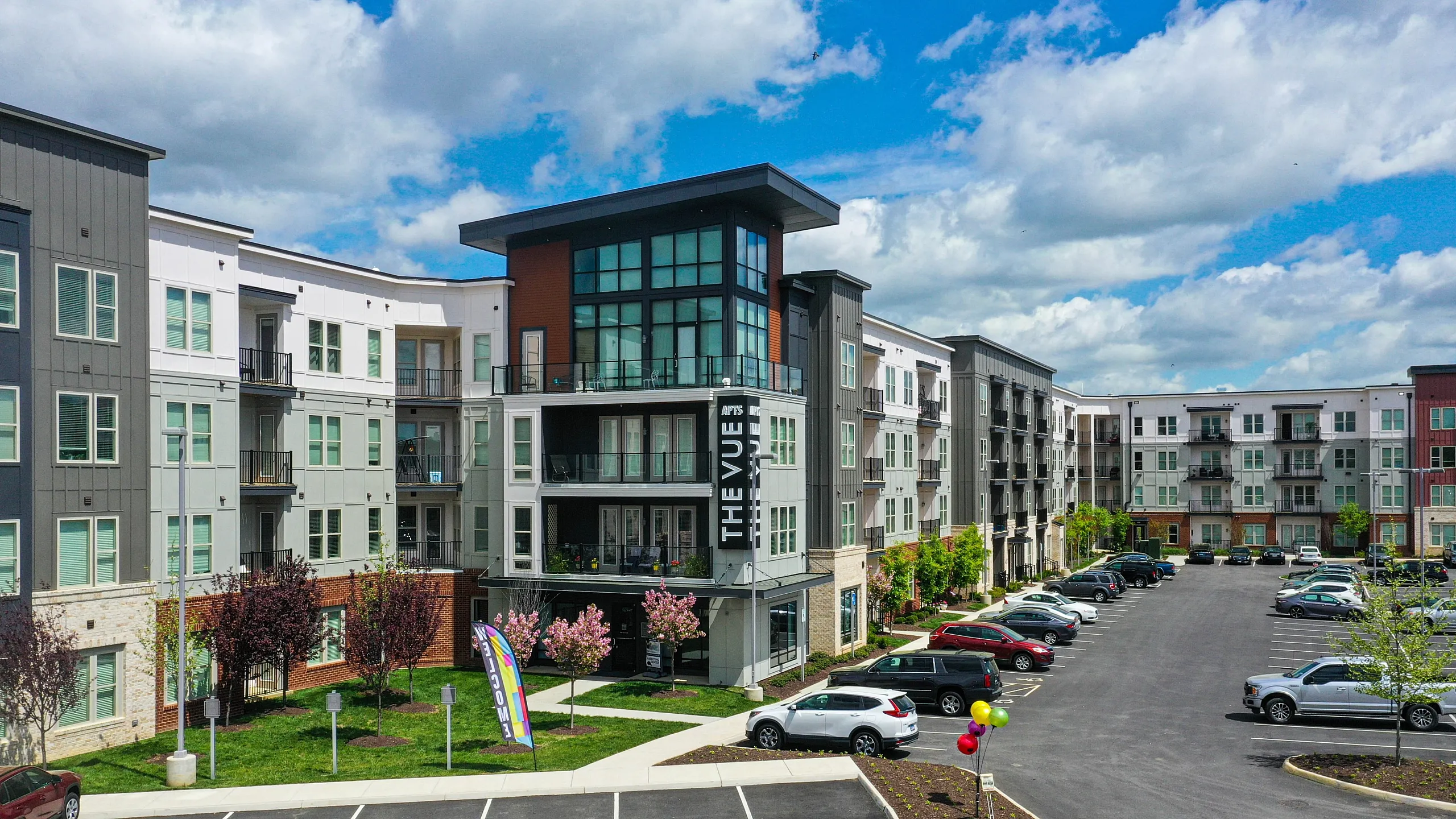 Modern multi-story apartment complex with sleek design, balconies, and ample parking.